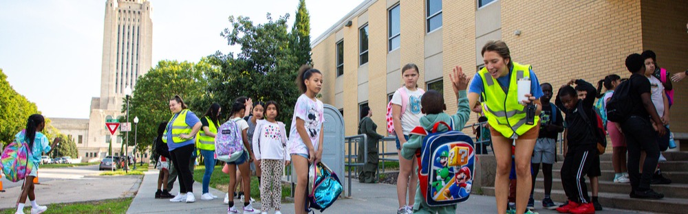Staff greet elementary students at McPhee with the state capitol building in the background.