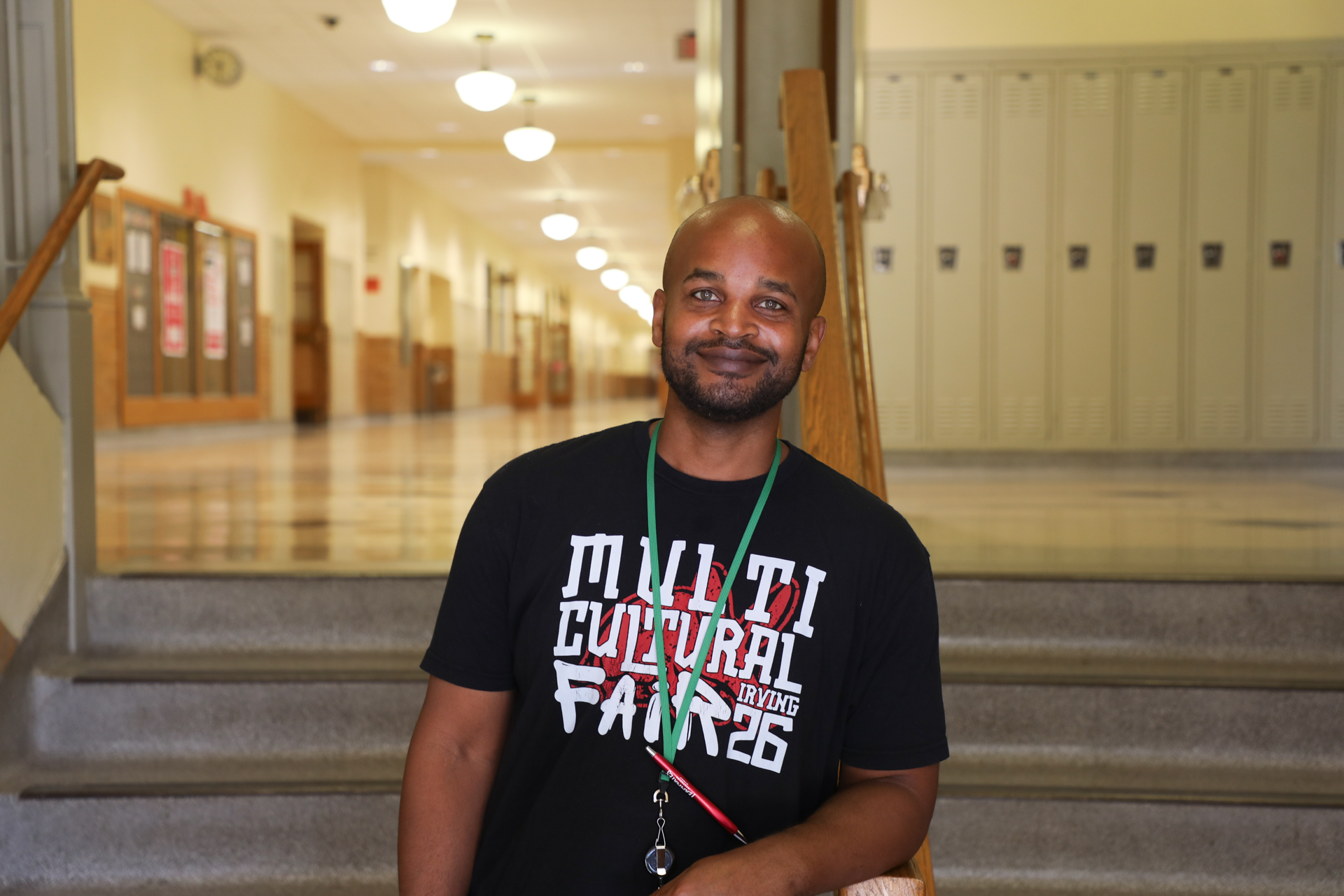 Man standing in stairway with lockers and school hallway in the background.