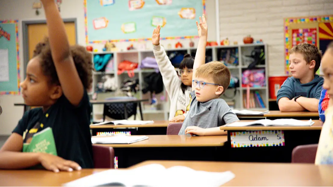 Students sitting at desks raising hands