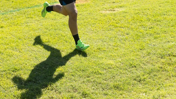 Runner’s legs and shadow on grassy field.