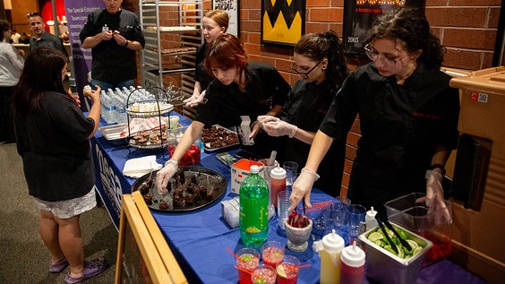 Students serving food at a school event table.