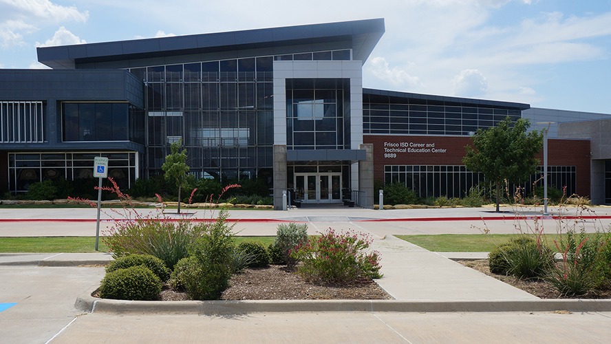 Exterior view of the CTE Center building on a bright, sunny day. The modern school facility is illuminated by clear blue skies and sunshine, with well-maintained landscaping and walkways visible in front of the building. The scene conveys a welcoming and professional educational environment.