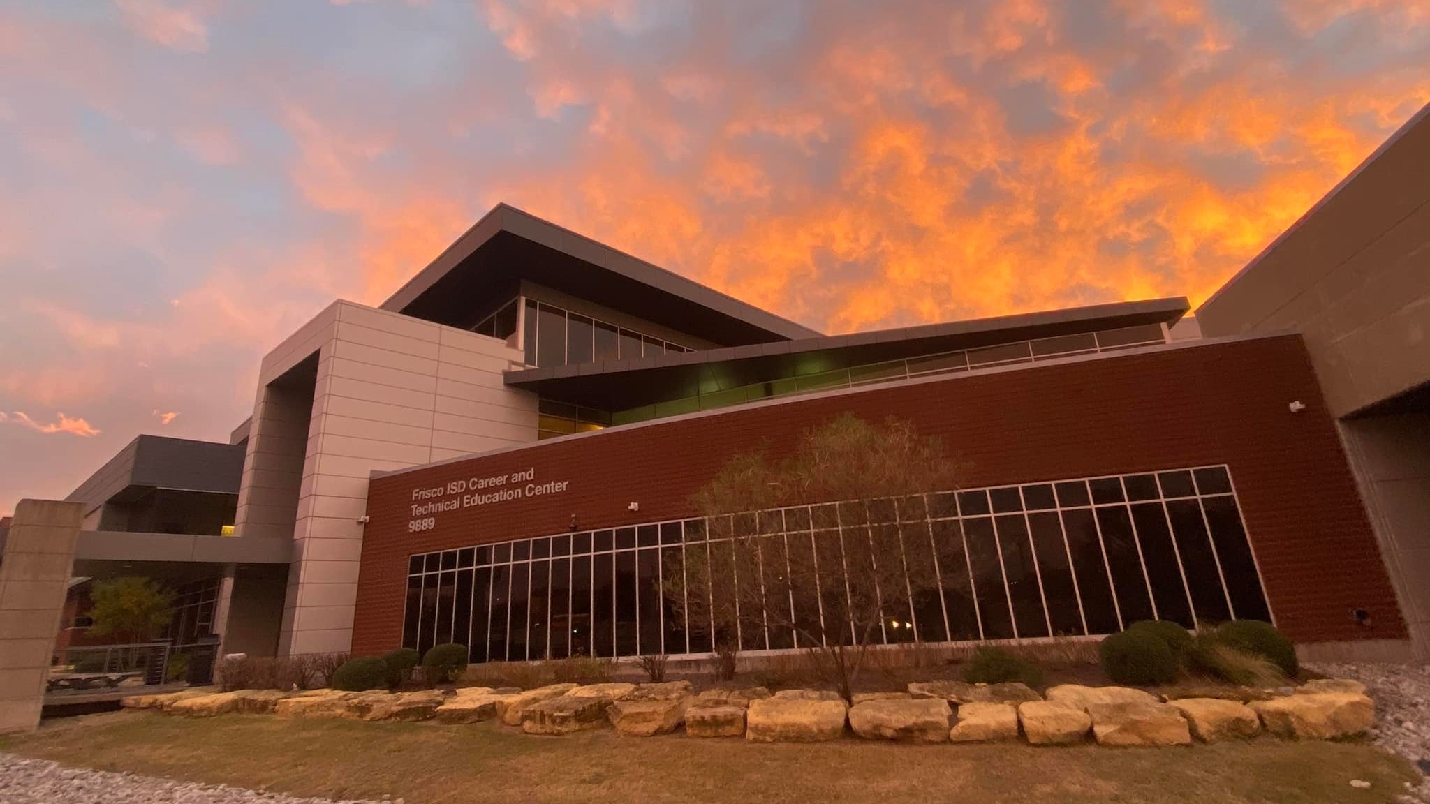 The exterior of the CTE Center is bathed in the warm glow of sunset beneath a dramatic sky of fiery orange and deep blue. Soft white clouds stretch across the horizon, creating a striking and picturesque backdrop for the campus building.