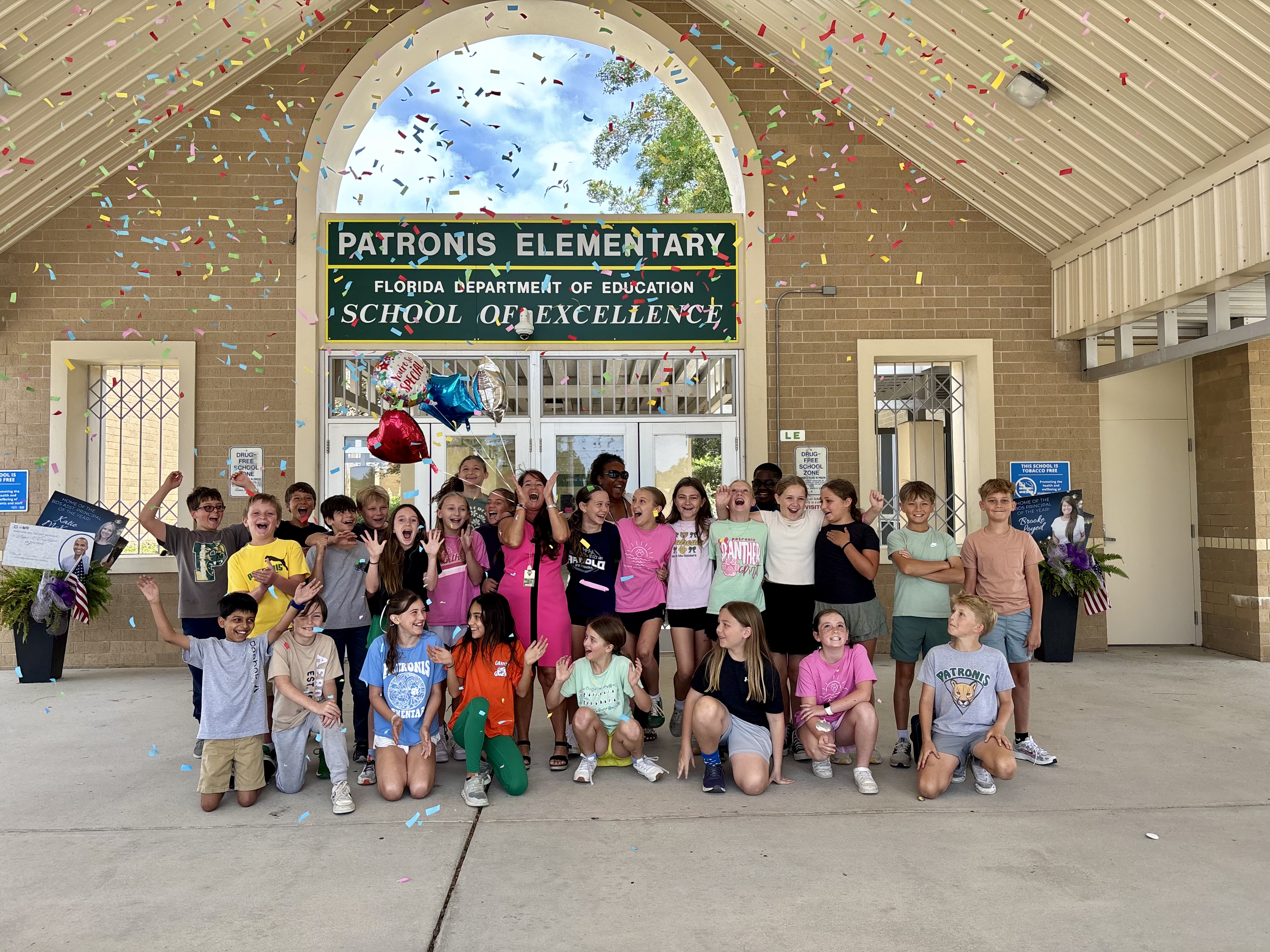 A group of students and adults smiling and cheering with confetti in the air.