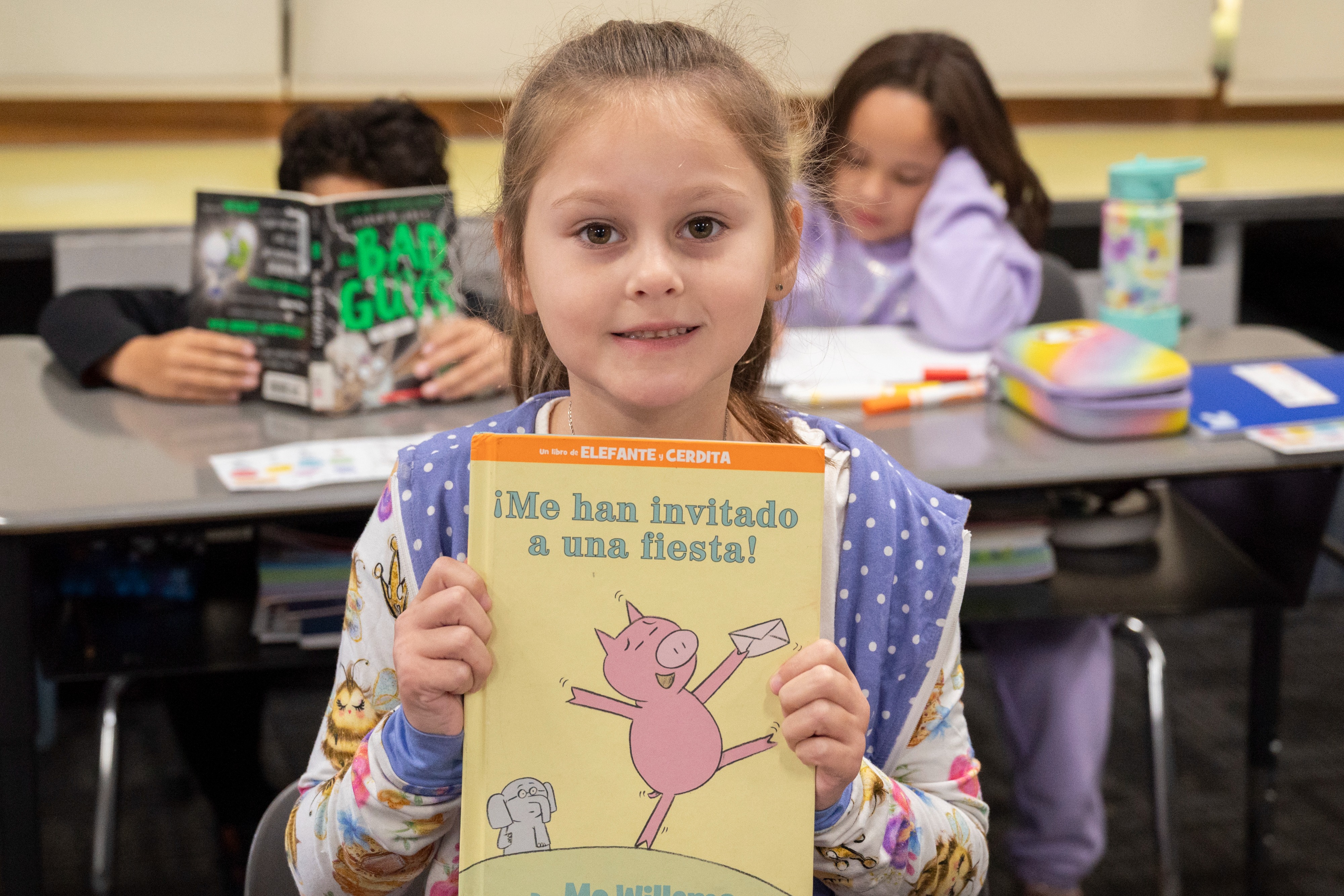 a girl holds up a book with a cover of a pig and elephant. The title is in Spanish
