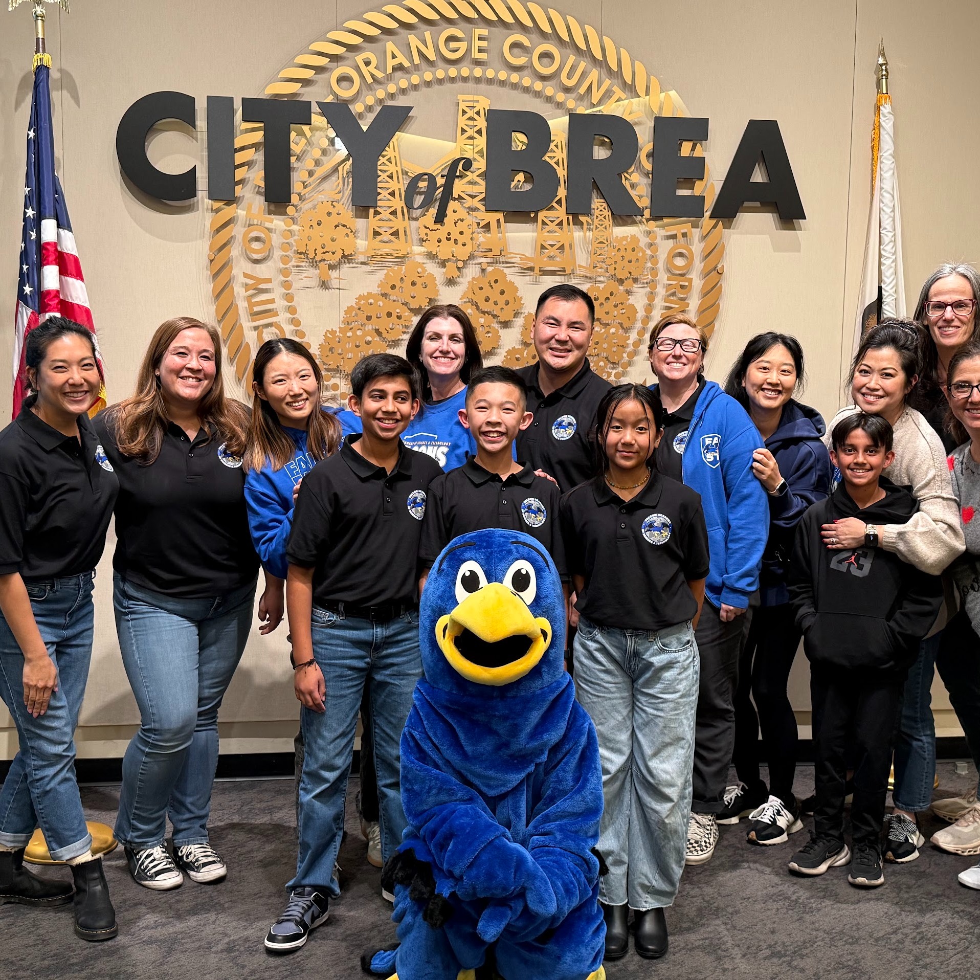 A group photo of educators and students standing with the Falcon mascot in front of a City of Brea sign