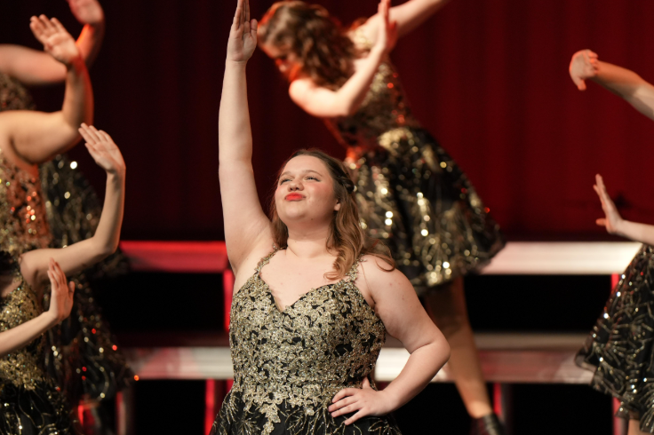 a girl dressed in a sequenced dress performs on stage with other girls 