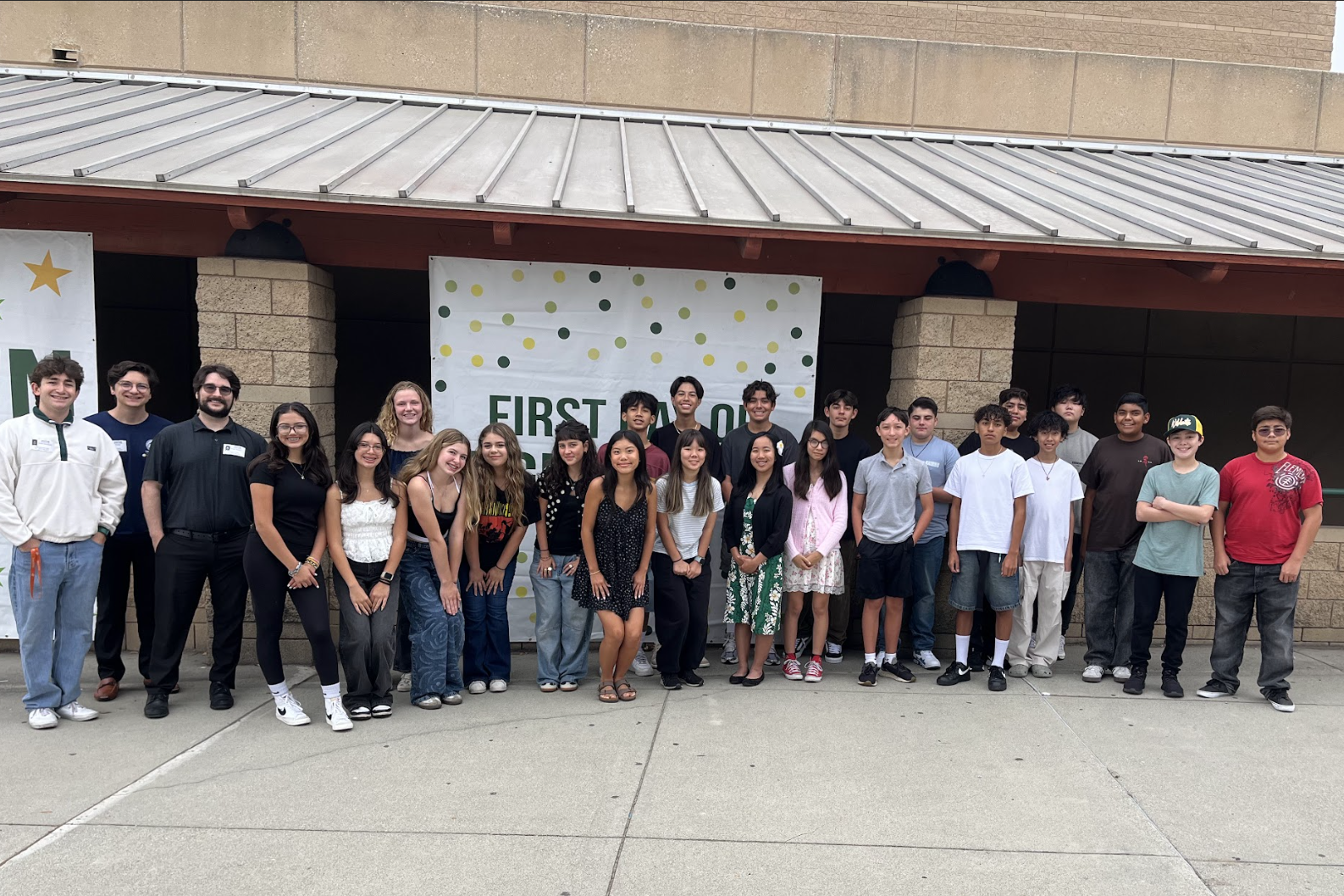 a group of freshmen stand with counselors in front of a white banner with green and gold dots
