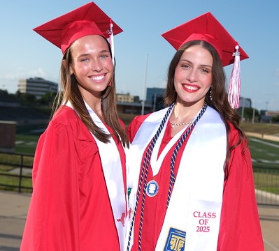 Two women in red caps and gowns stand at an outdoor stadium. One wears a sash with "Class of 2022."