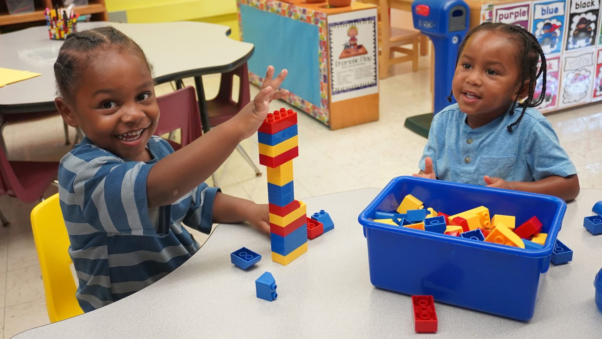 Two preschool children at a table smiliing stacking colorful blocks