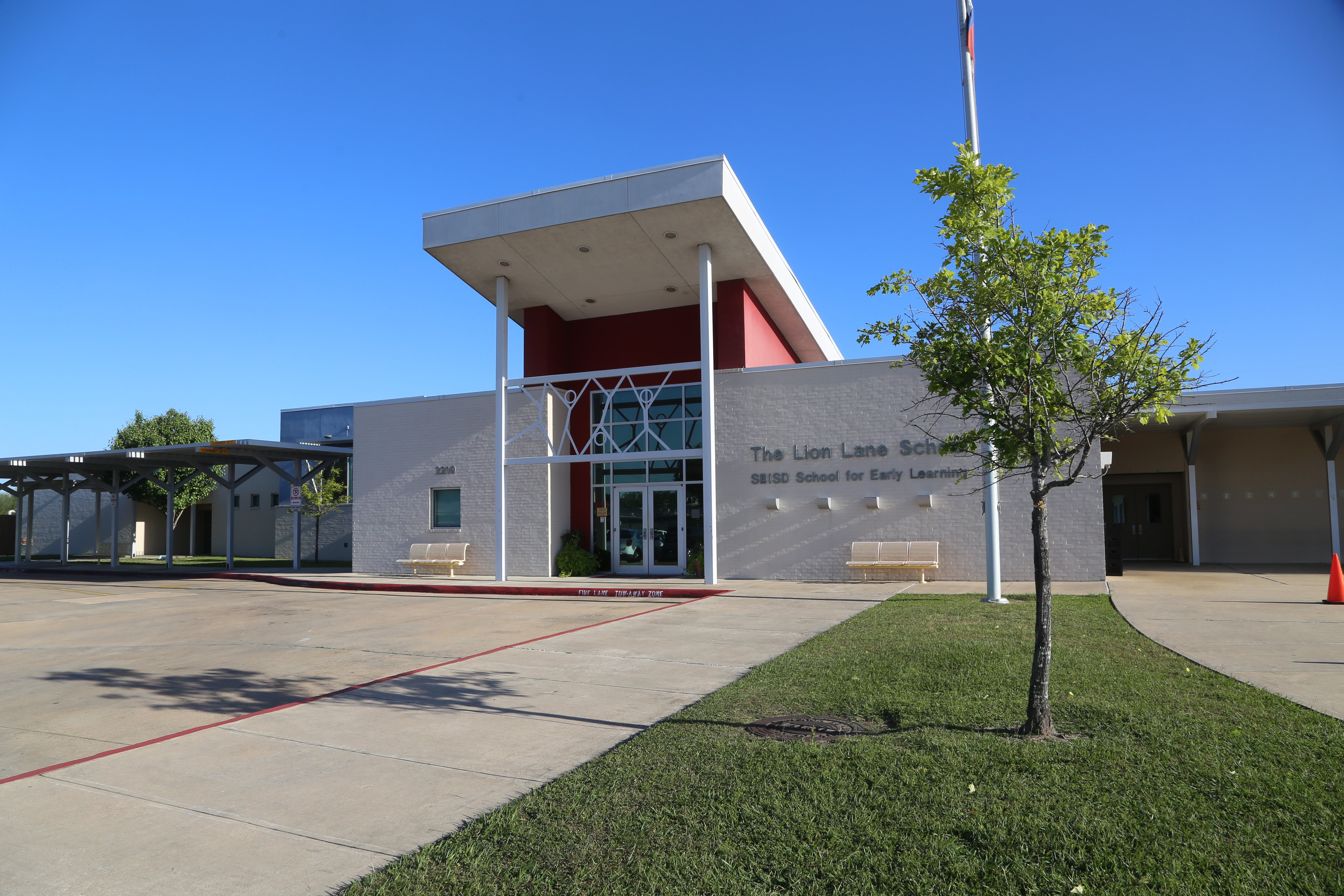 Exterior of a modern building with glass doors, red trim, and a flag. Two benches on either side.