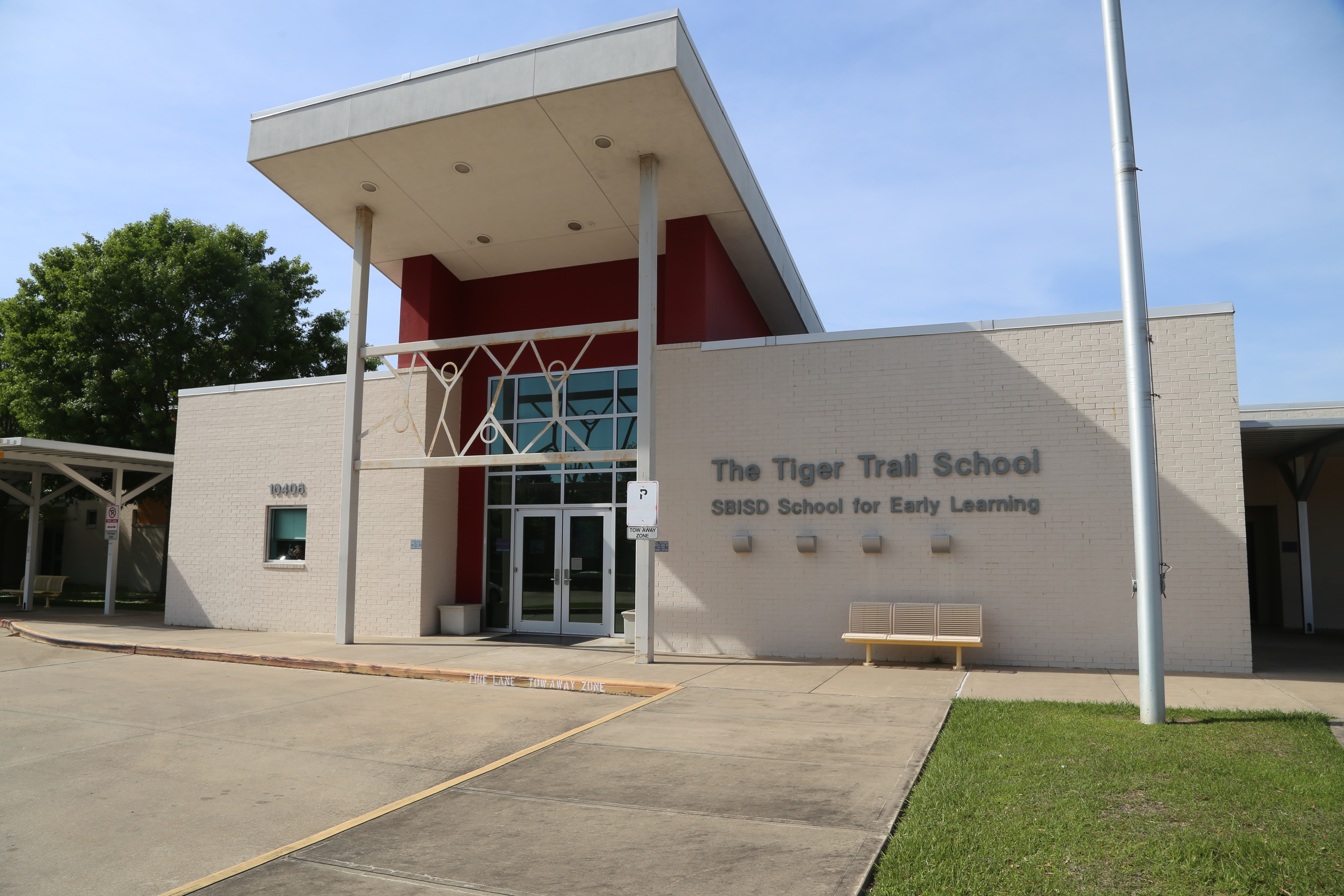 Entrance to Tiger Trail School with red trim, glass doors, bench, and grassy lawn in front.