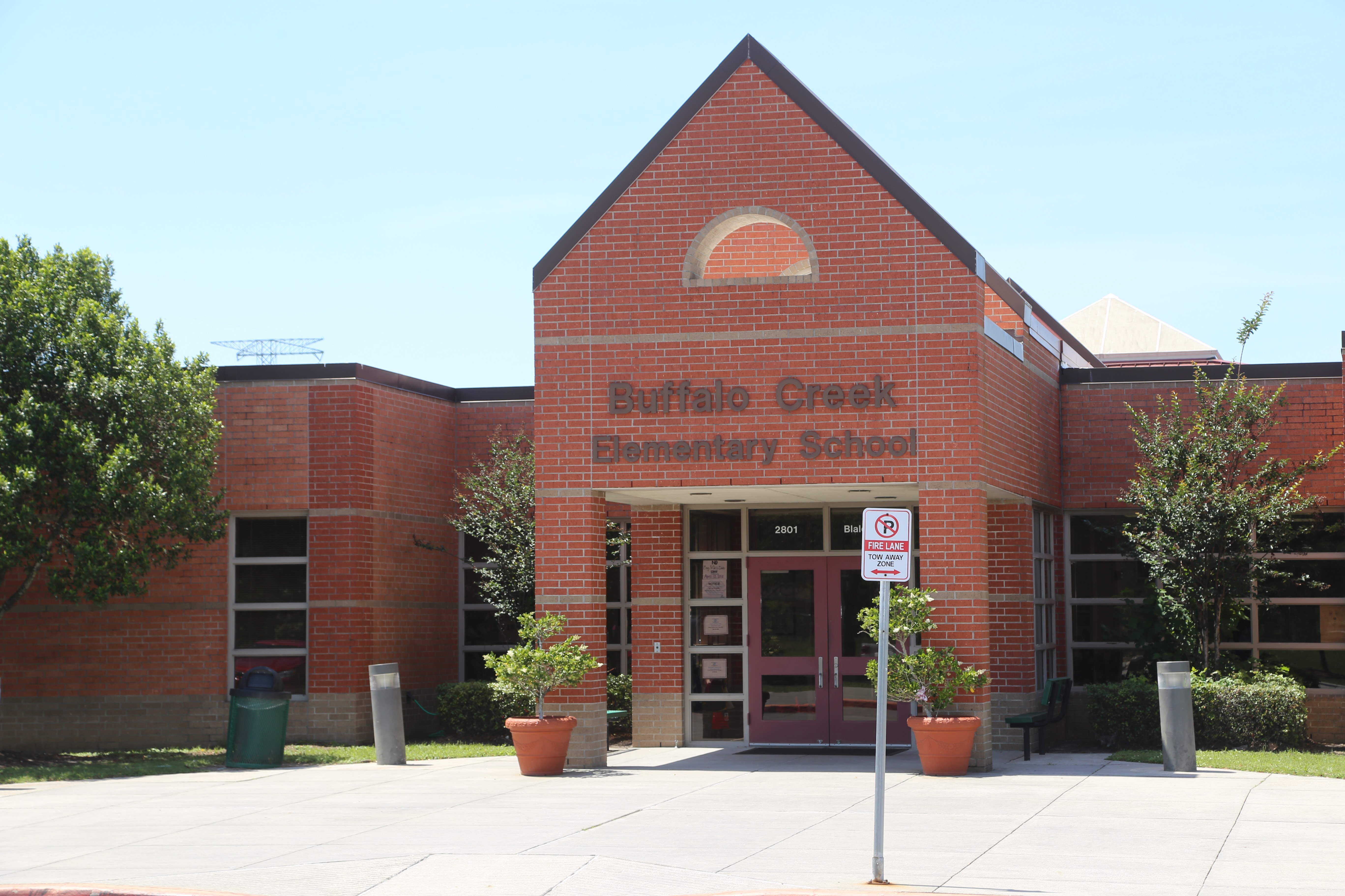 Entrance to Buffalo Creek Elementary School with a brick facade, arched window, red door, and two potted plants.