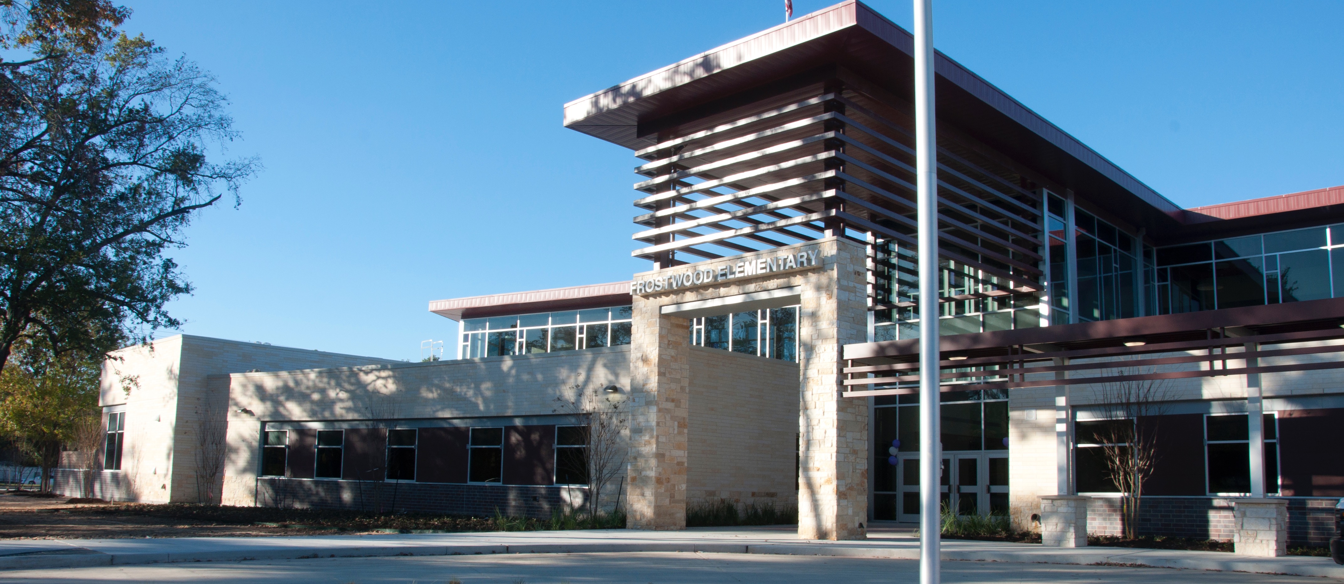 A modern building with glass windows and a flag atop a tall flagpole in front of a landscaped area.