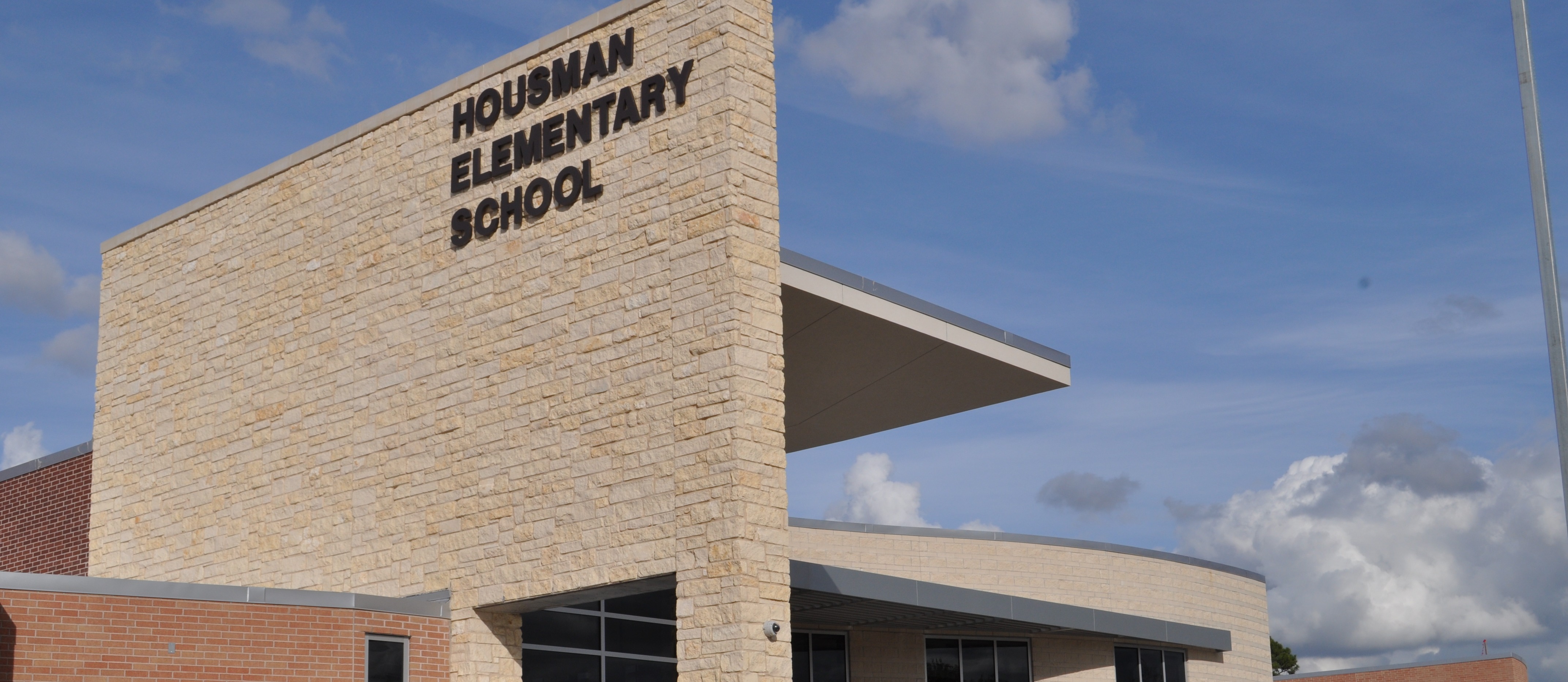 Exterior of Hourman Elementary School, brick walls, glass windows, arched entrance, and cloudy sky background.