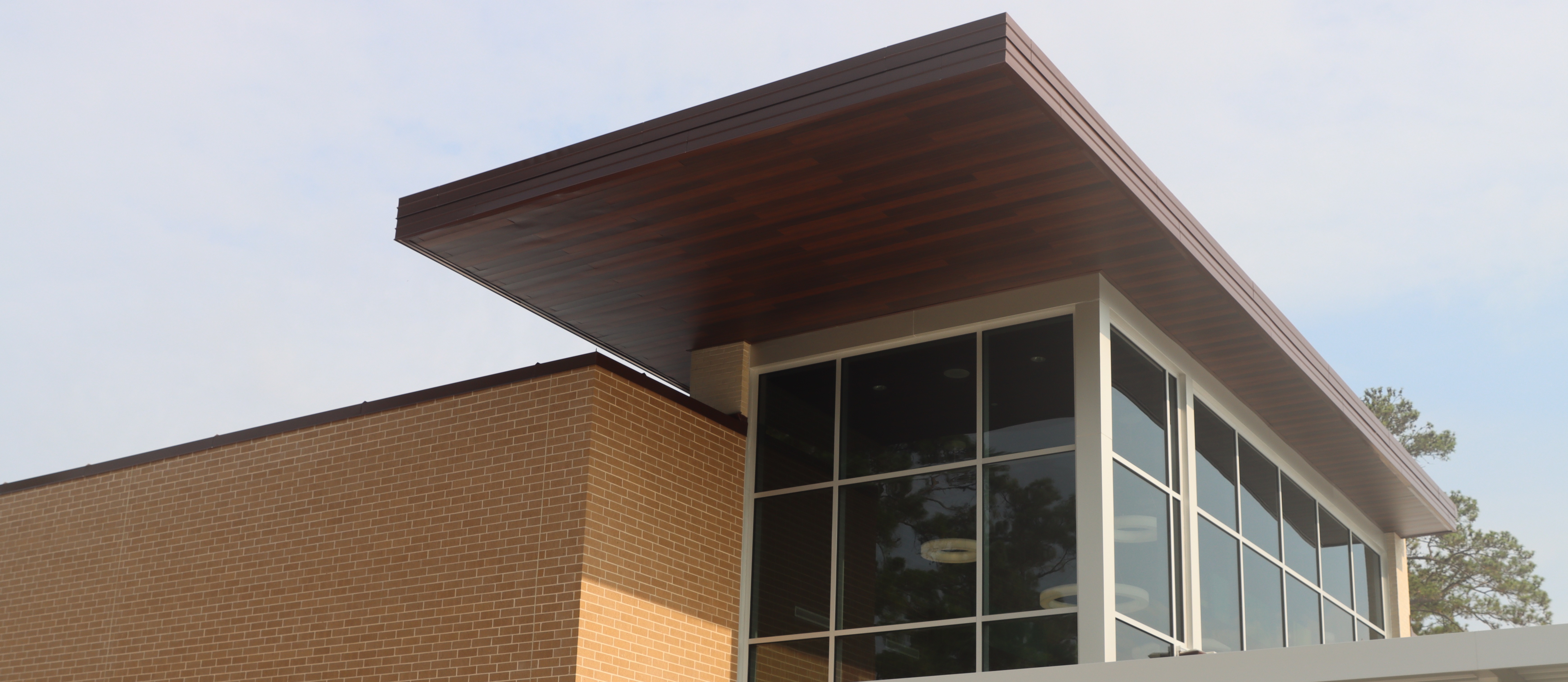 A modern building with a slanted roof and glass windows. The front features a canopy and an entrance with double doors.