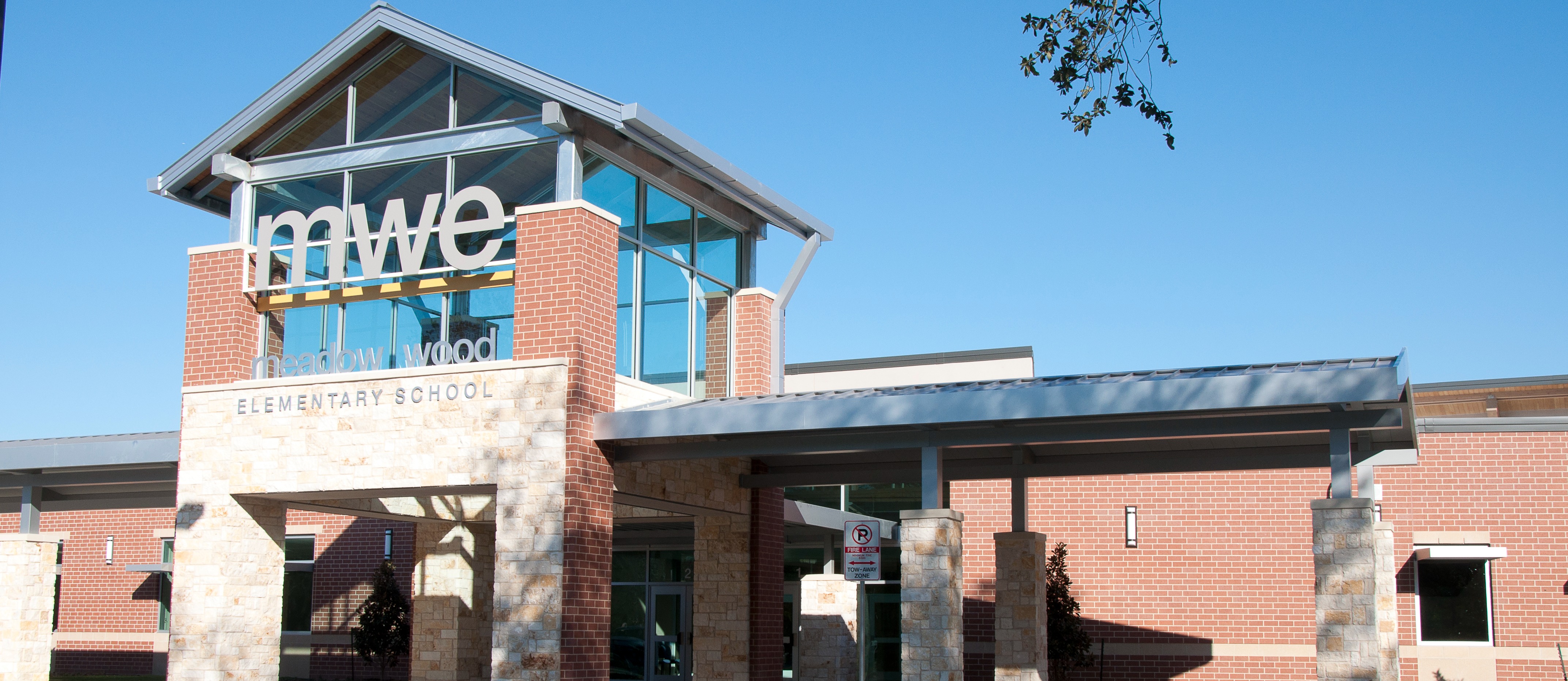 Modern building with a glass entrance and a brick facade. Name "lmwe" in orange letters above entrance.