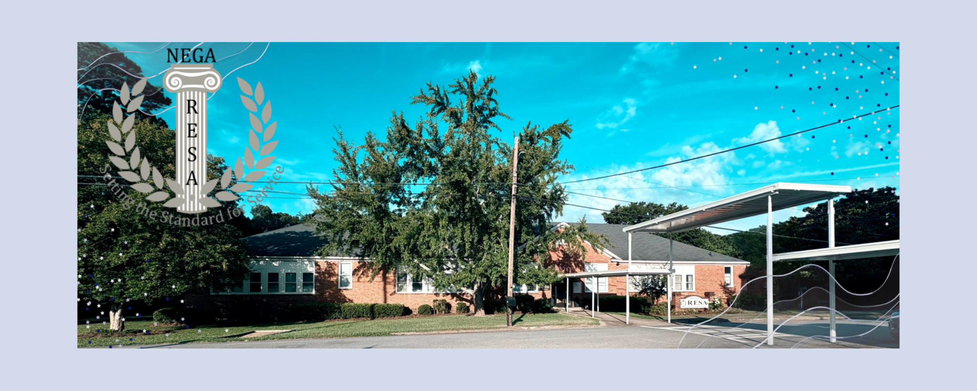 A building with a carport stands in a yard with trees. A sign with letters and symbols is on the left.