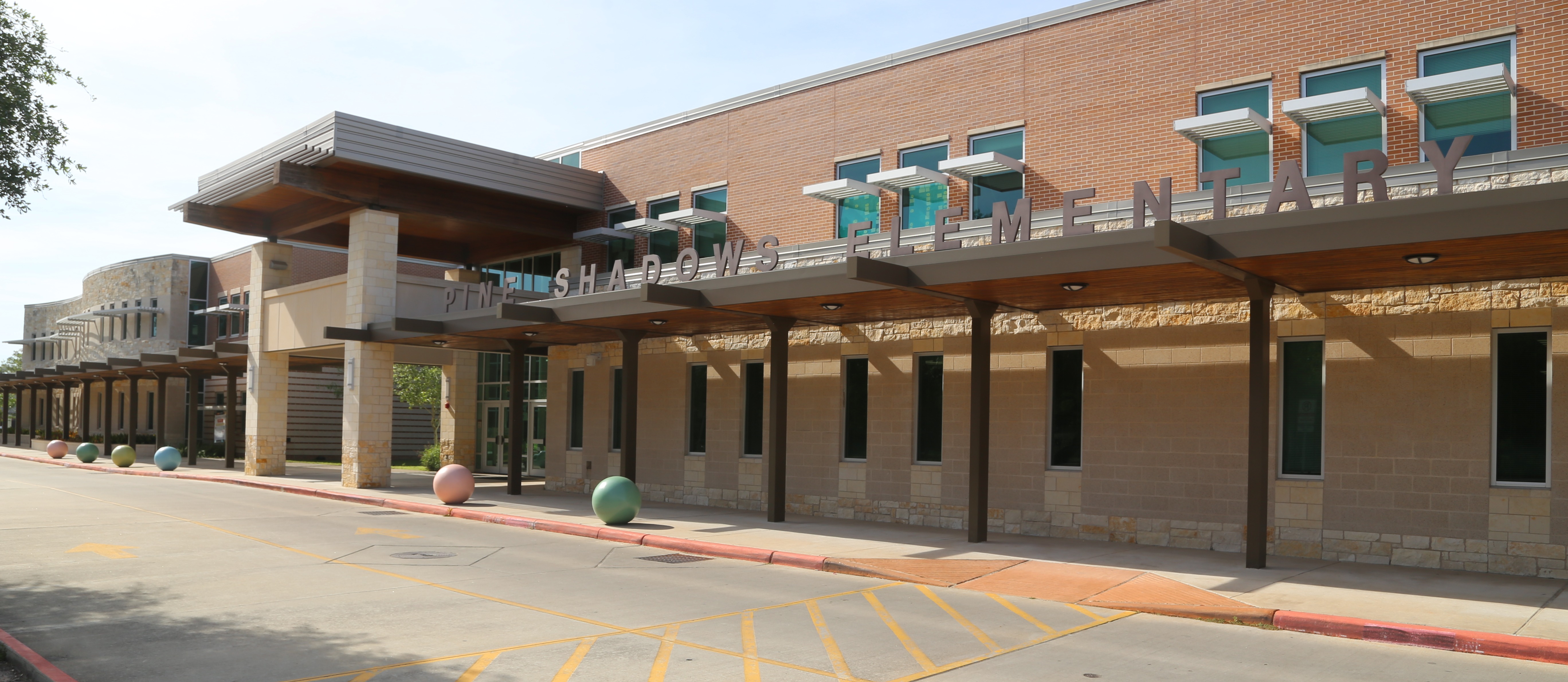 An empty parking lot in front of a brick elementary school building with glass windows and awnings.