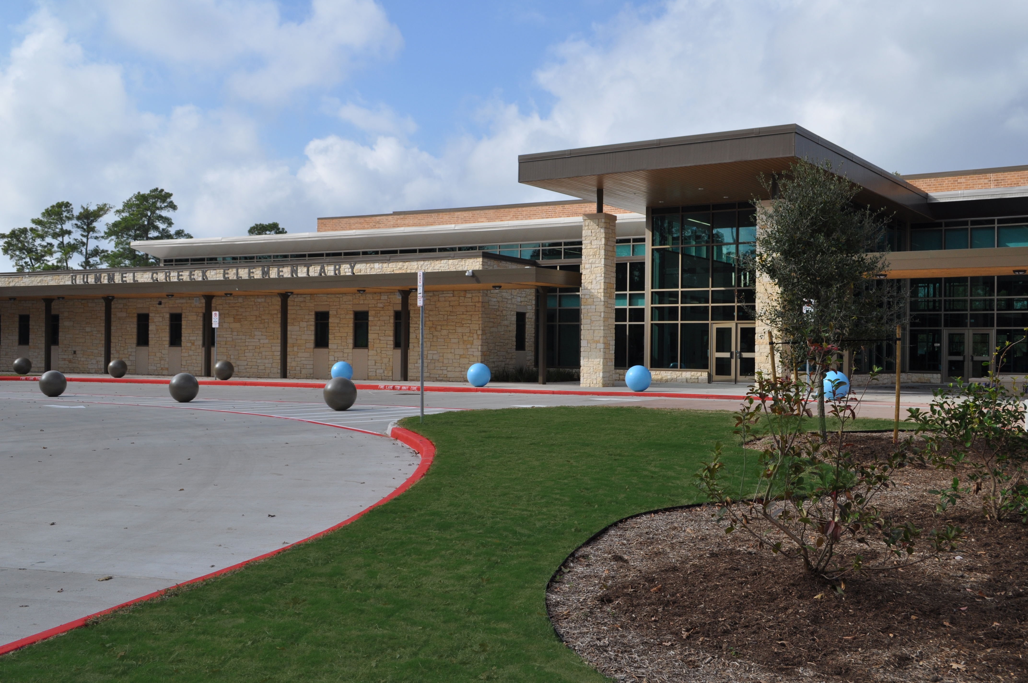A modern building with a curved roof and glass windows. A red stripe marks the driveway. Several gray and blue spheres are scattered.