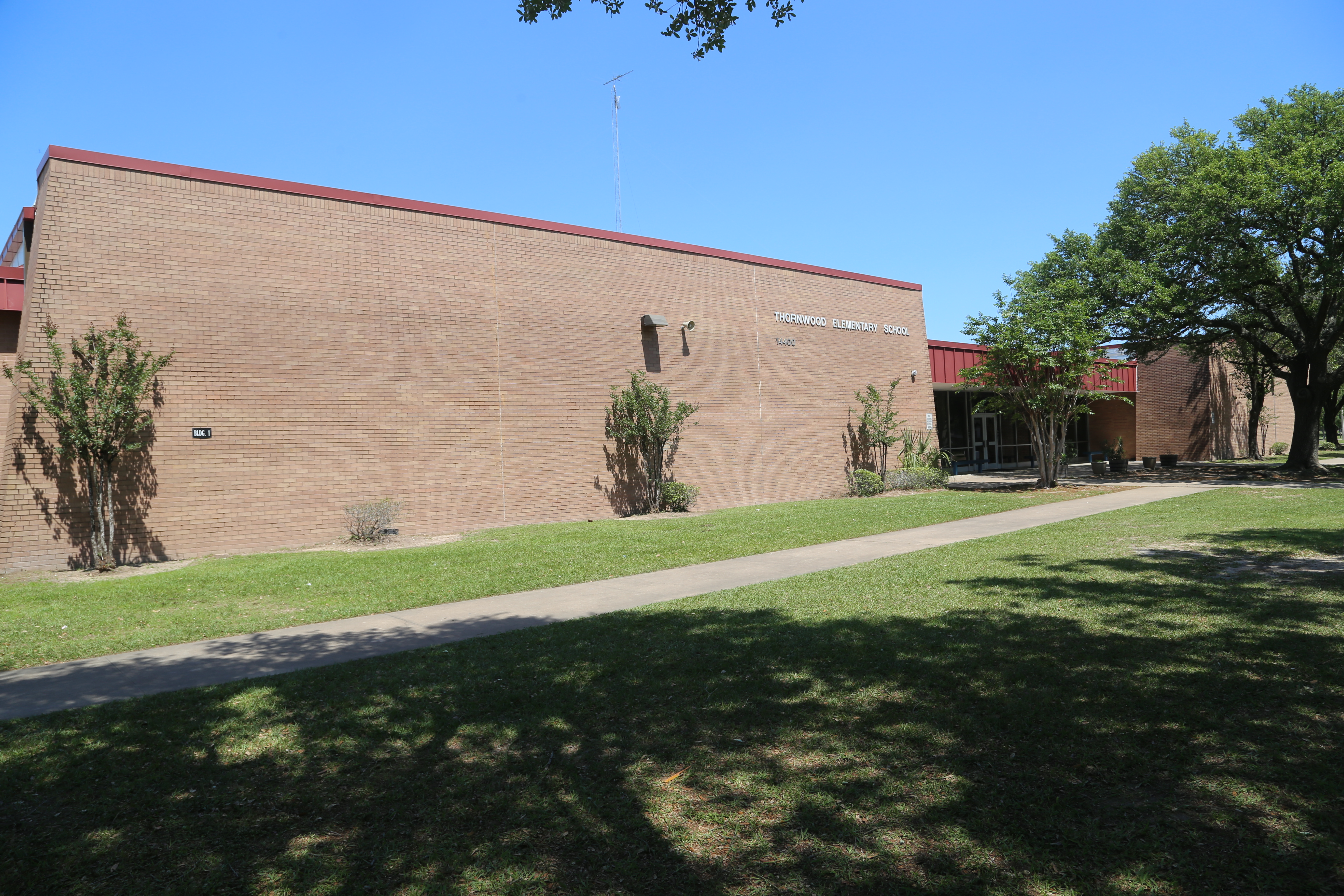 A building with a red roof has a grassy lawn in front with a walkway. Shrubs and trees are near the building.