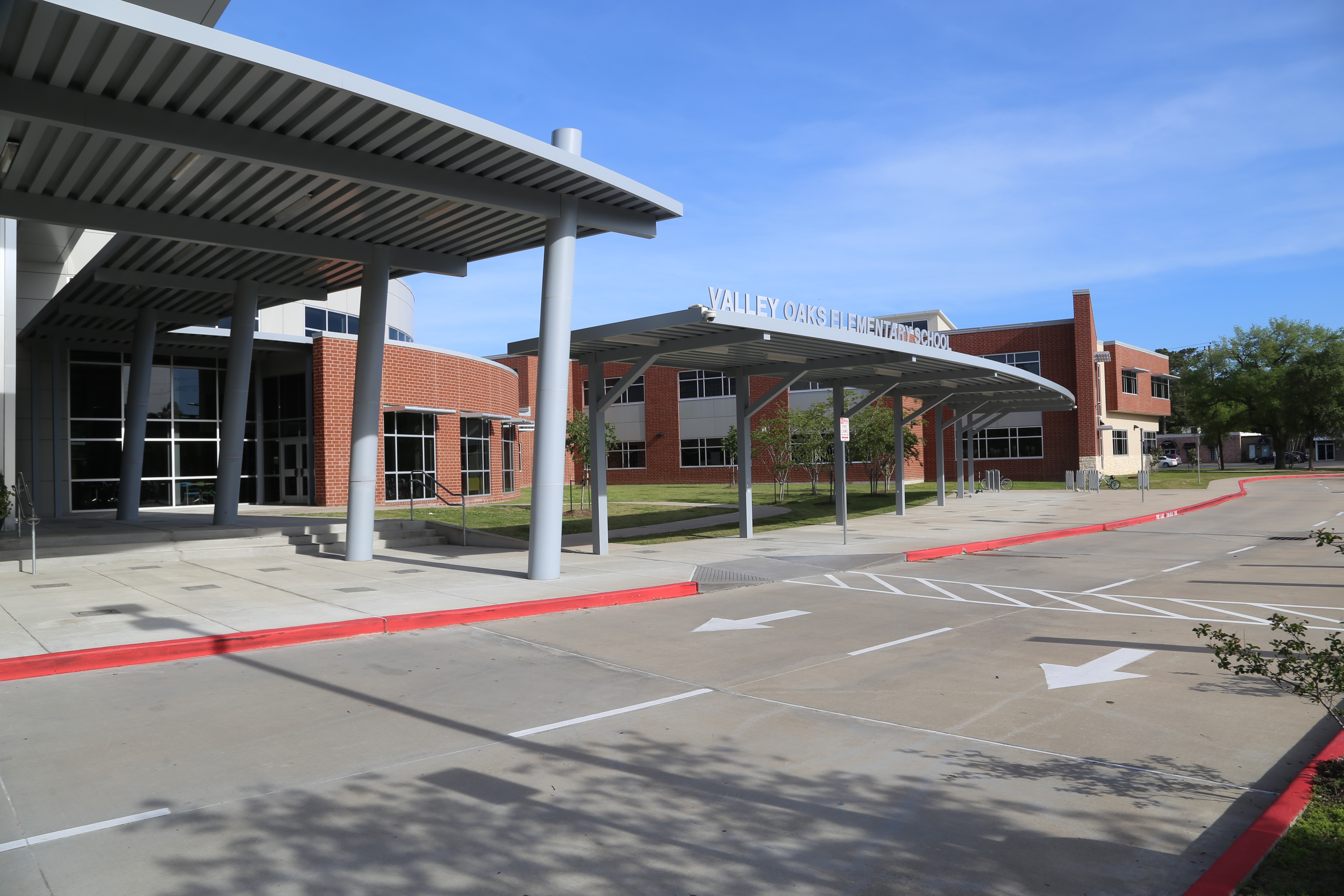 An empty parking lot with red lines, large awning, and metal supports. Behind the awning is a building.