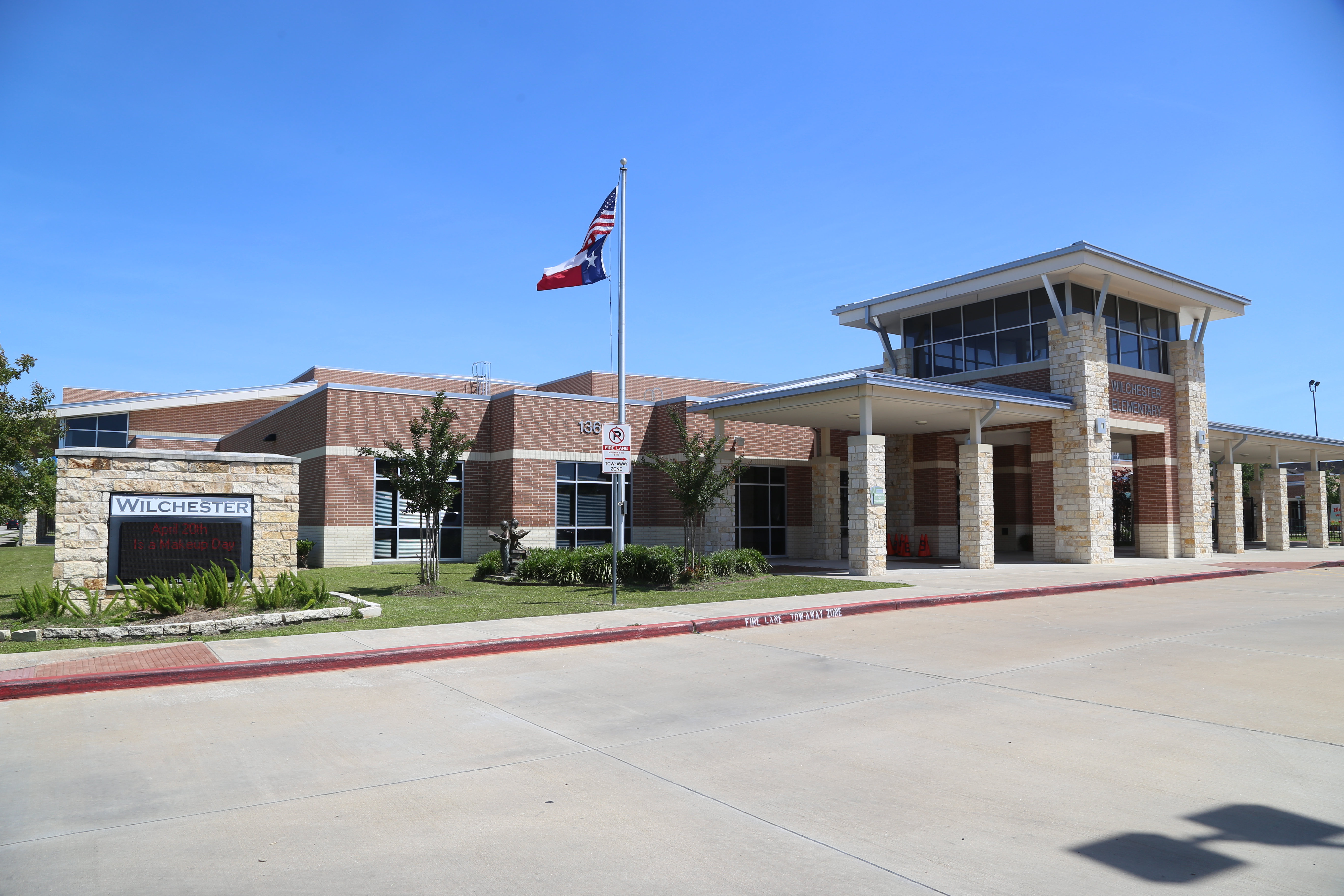 A school building with flag, brick walls, glass windows, and a grassy area in front.