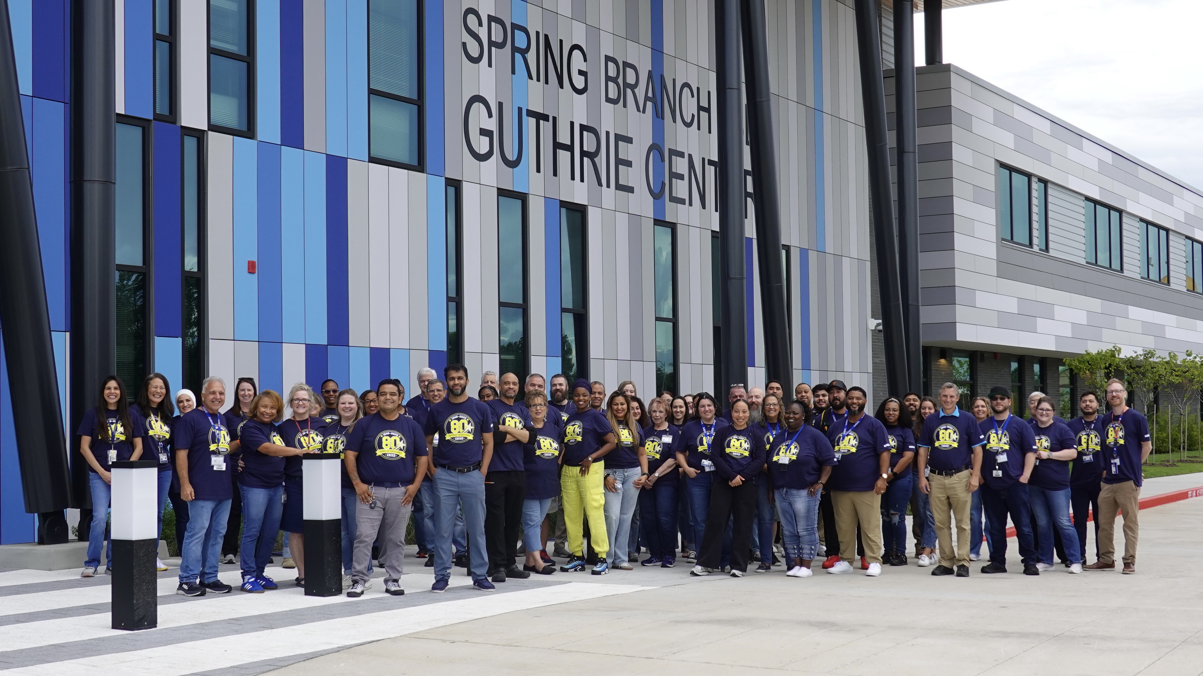 Large group of people wearing matching blue shirts standing in front of a building with "Spring Branch Guthrie Center" on it.