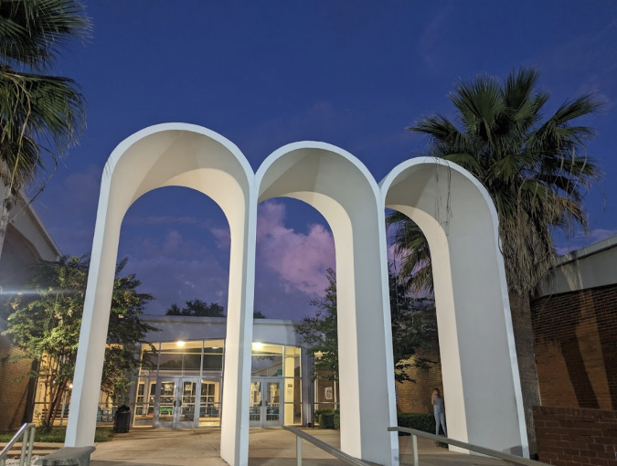 Entrance with three curved arches, a concrete walkway, and palm trees under a clear evening sky.