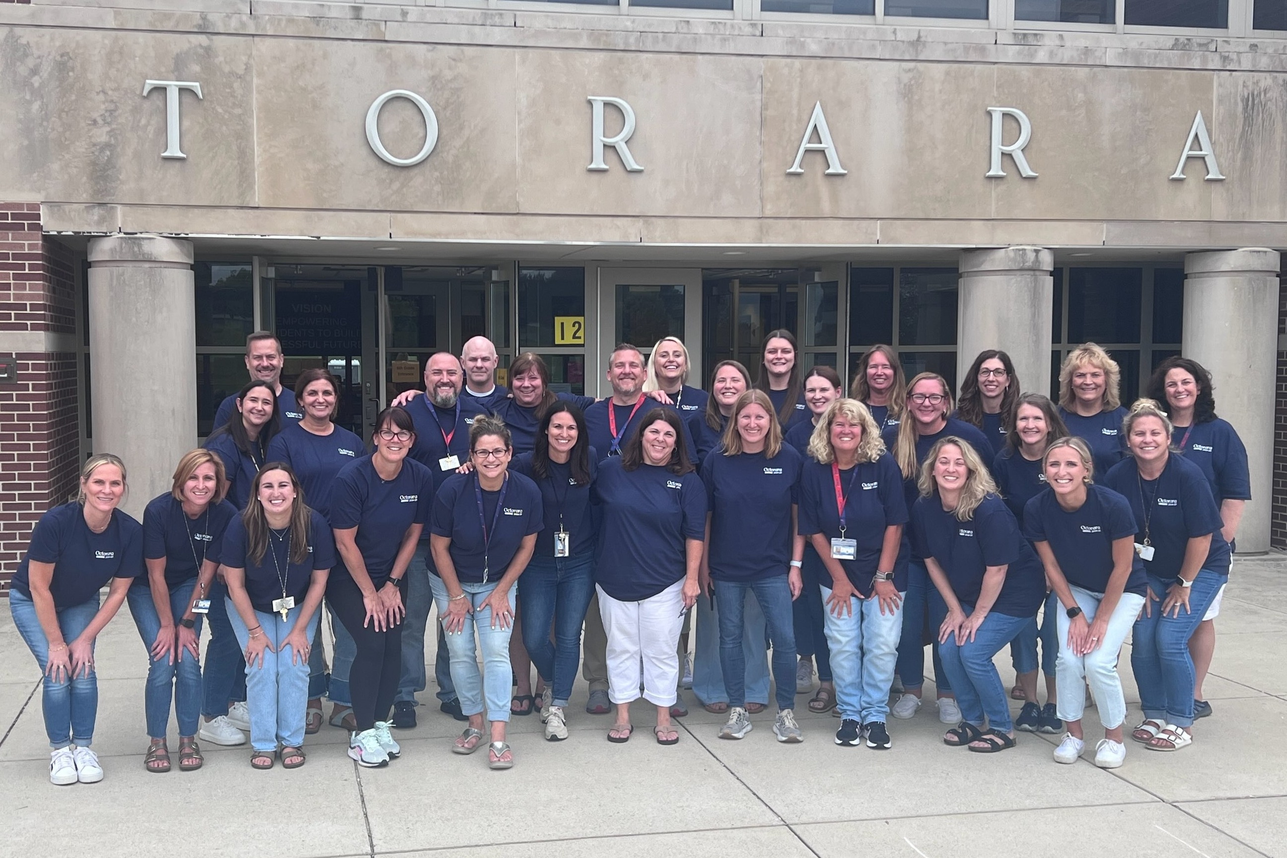 staff posing in front of school