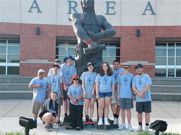 students pose in blue t-shirts in front of Brave statue