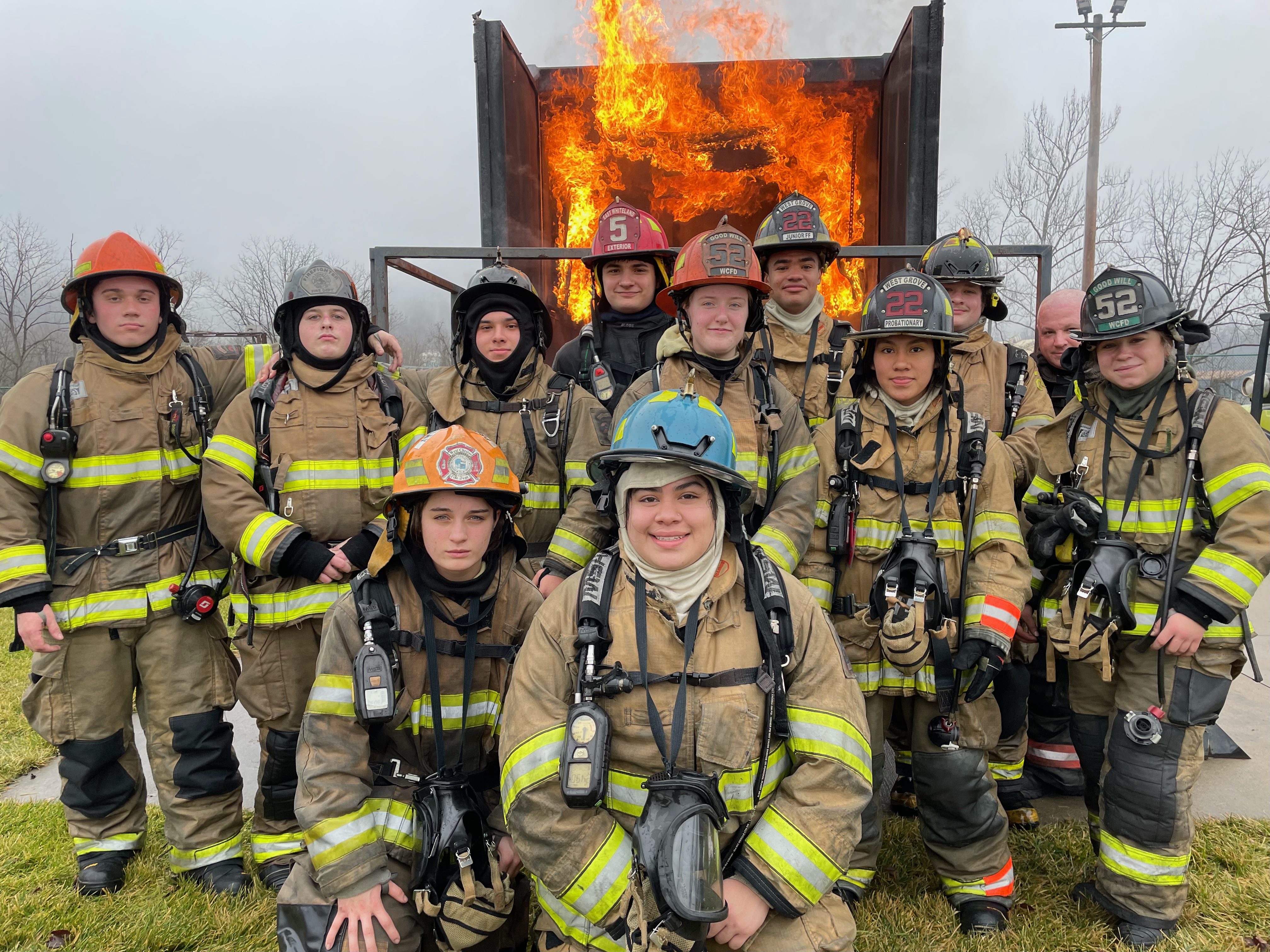 firefighter students in their uniforms posing in front of contained fire