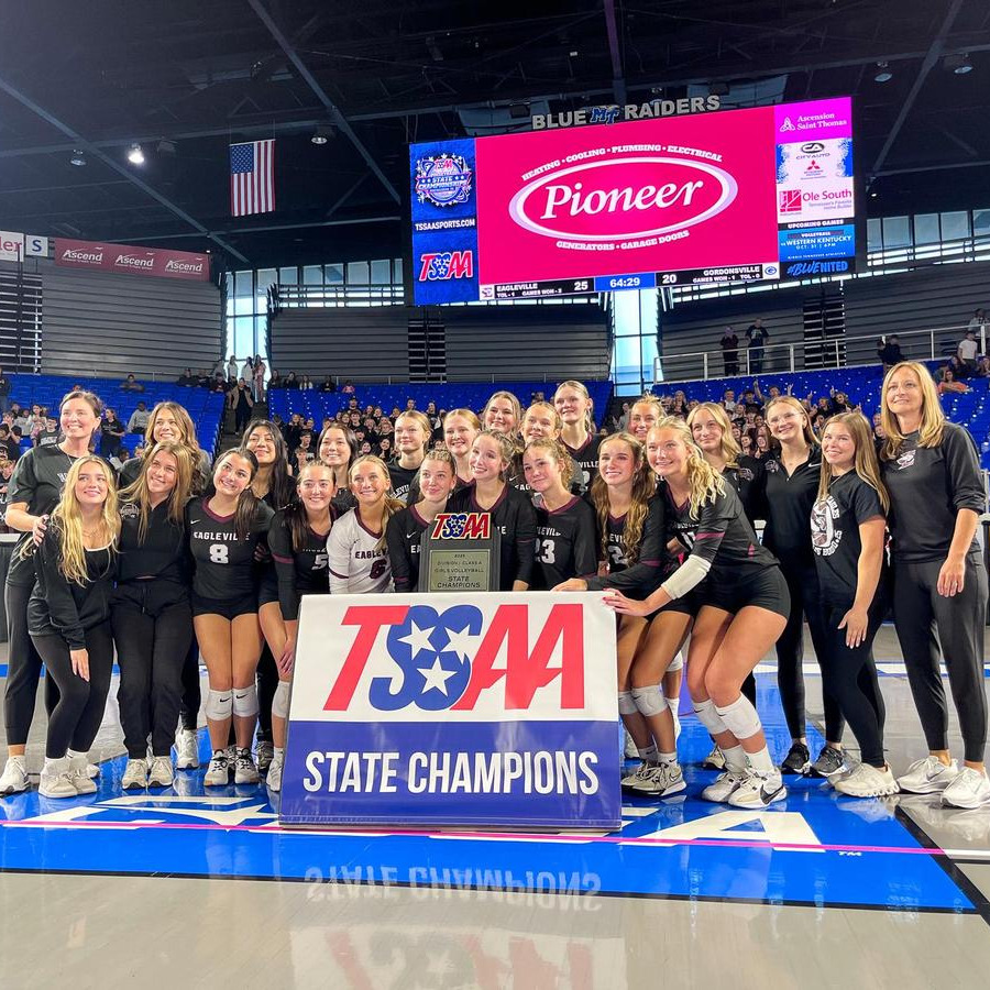 A group of women in matching black uniforms stands with a large sign that says "TSAM State Champions."
