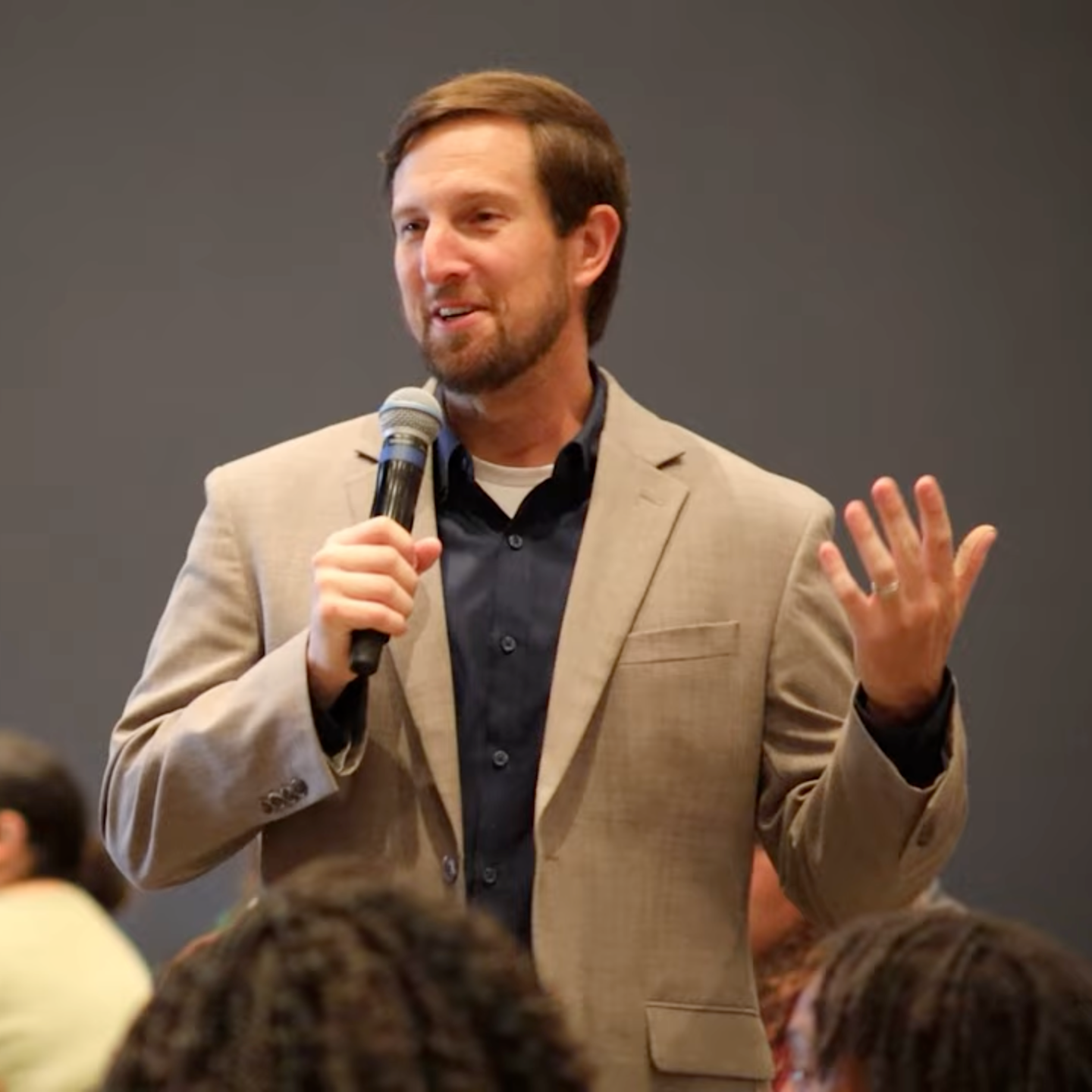 Man in tan suit speaks to crowd of teachers