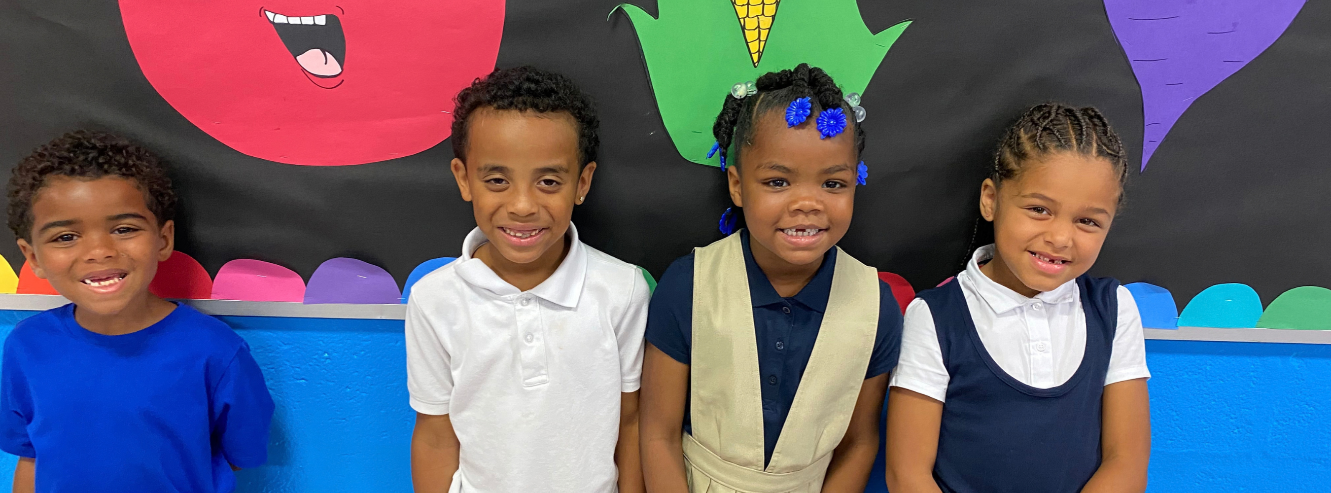 Four students smiling against a colorful bulletin board