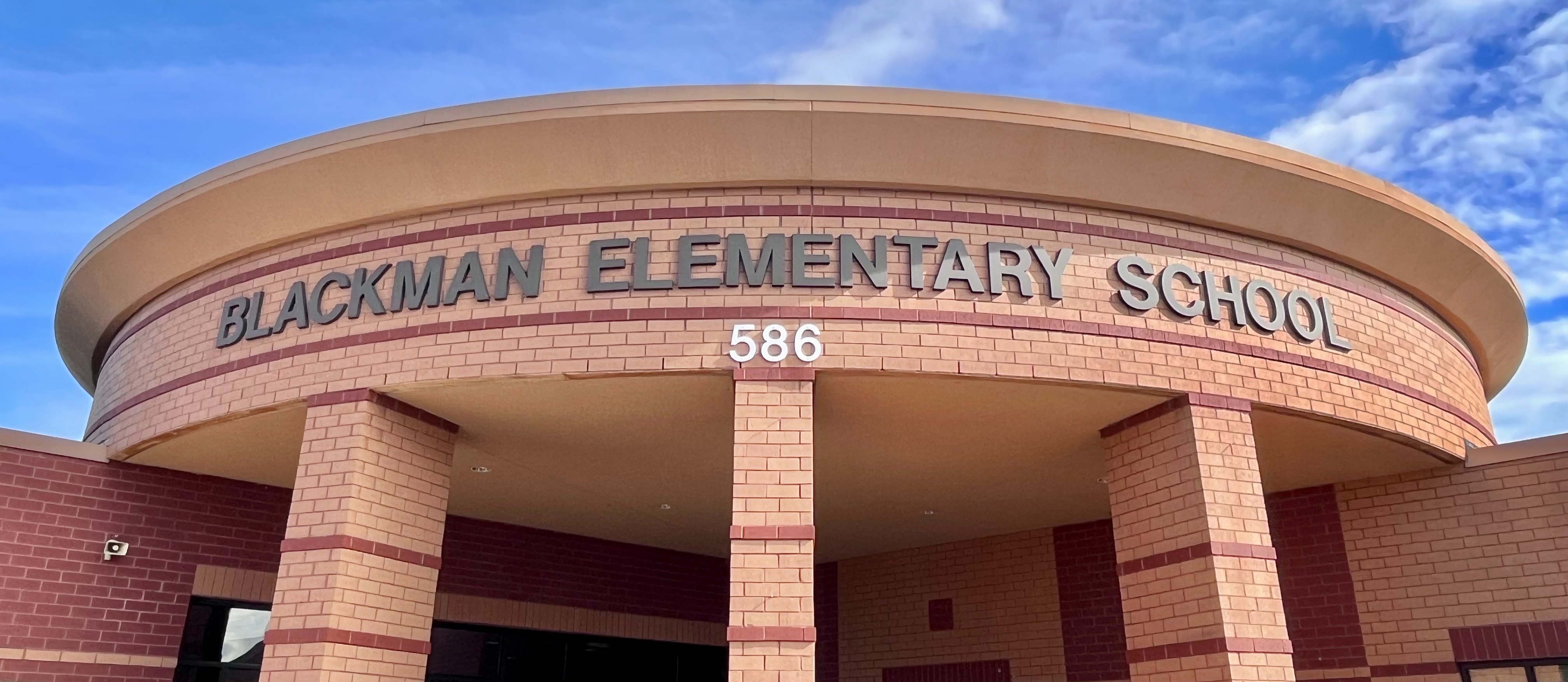 Front entrance of Blackman Elementary School with a circular arch, brick pillars, and a blue sky with clouds.