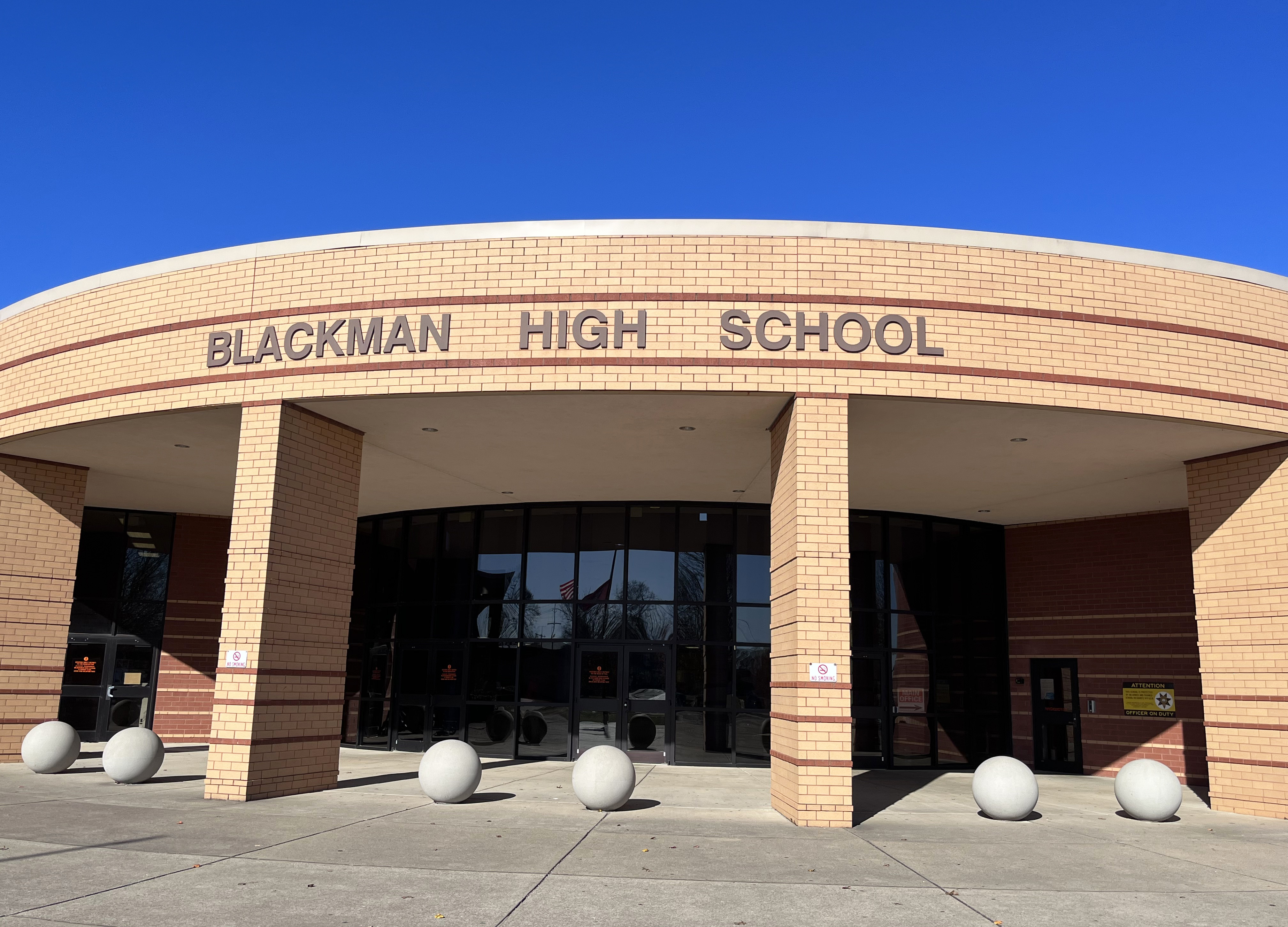 A high school entrance with a curved brick facade, white lettering reading "BLACKMAN HIGH SCHOOL," and large white spheres in front.