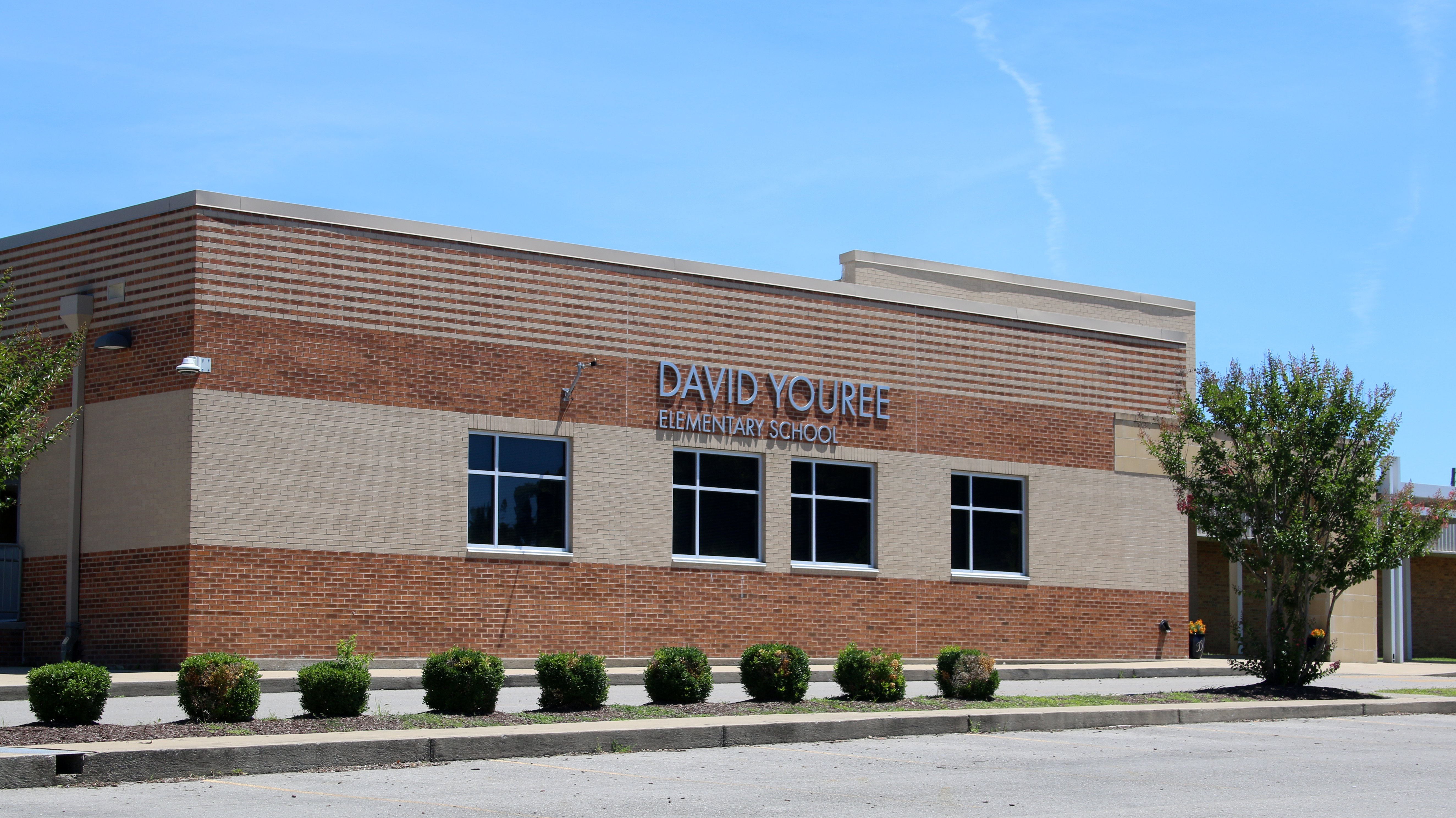 A two-story brick building with windows, labeled "DAVID YOUREE ELEMENTARY SCHOOL," has greenery in the front.