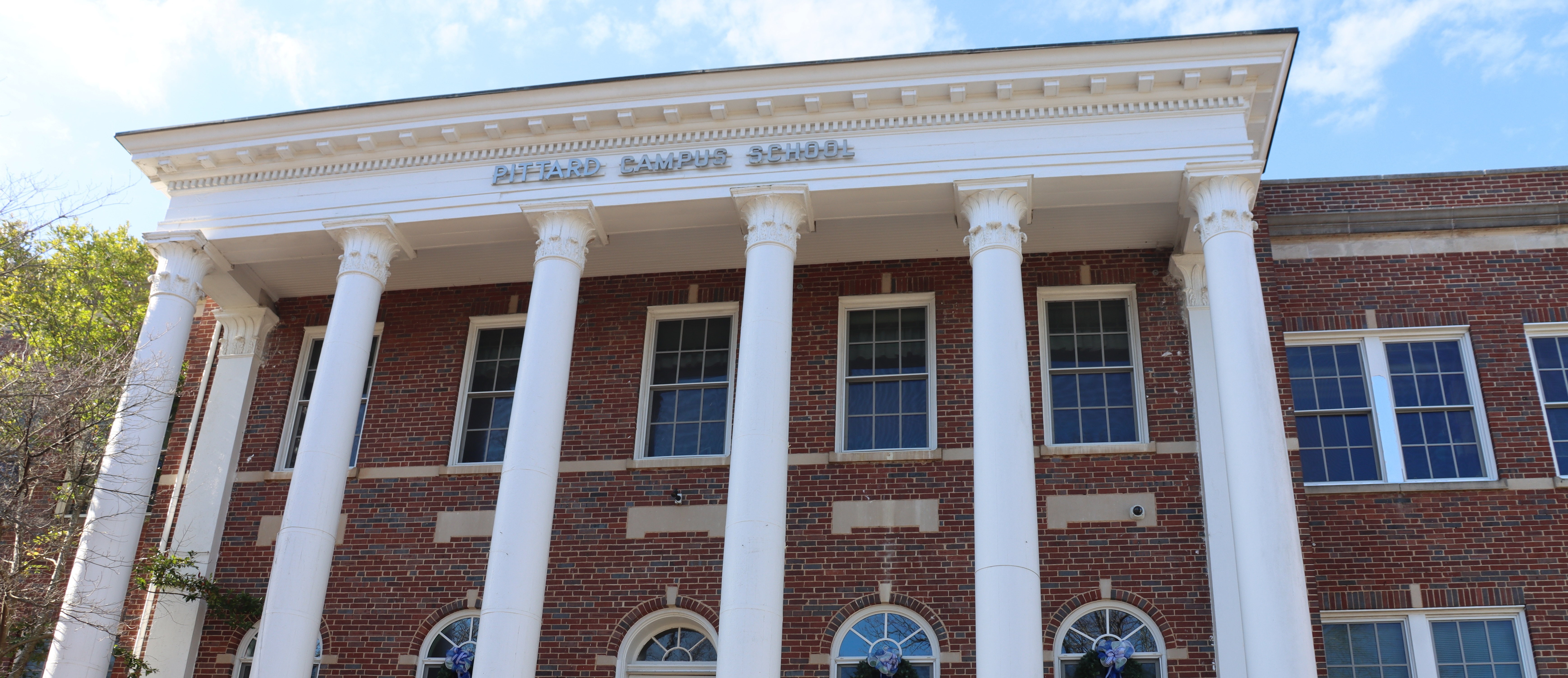 A brick building with white columns and arched windows, under a blue sky with clouds.