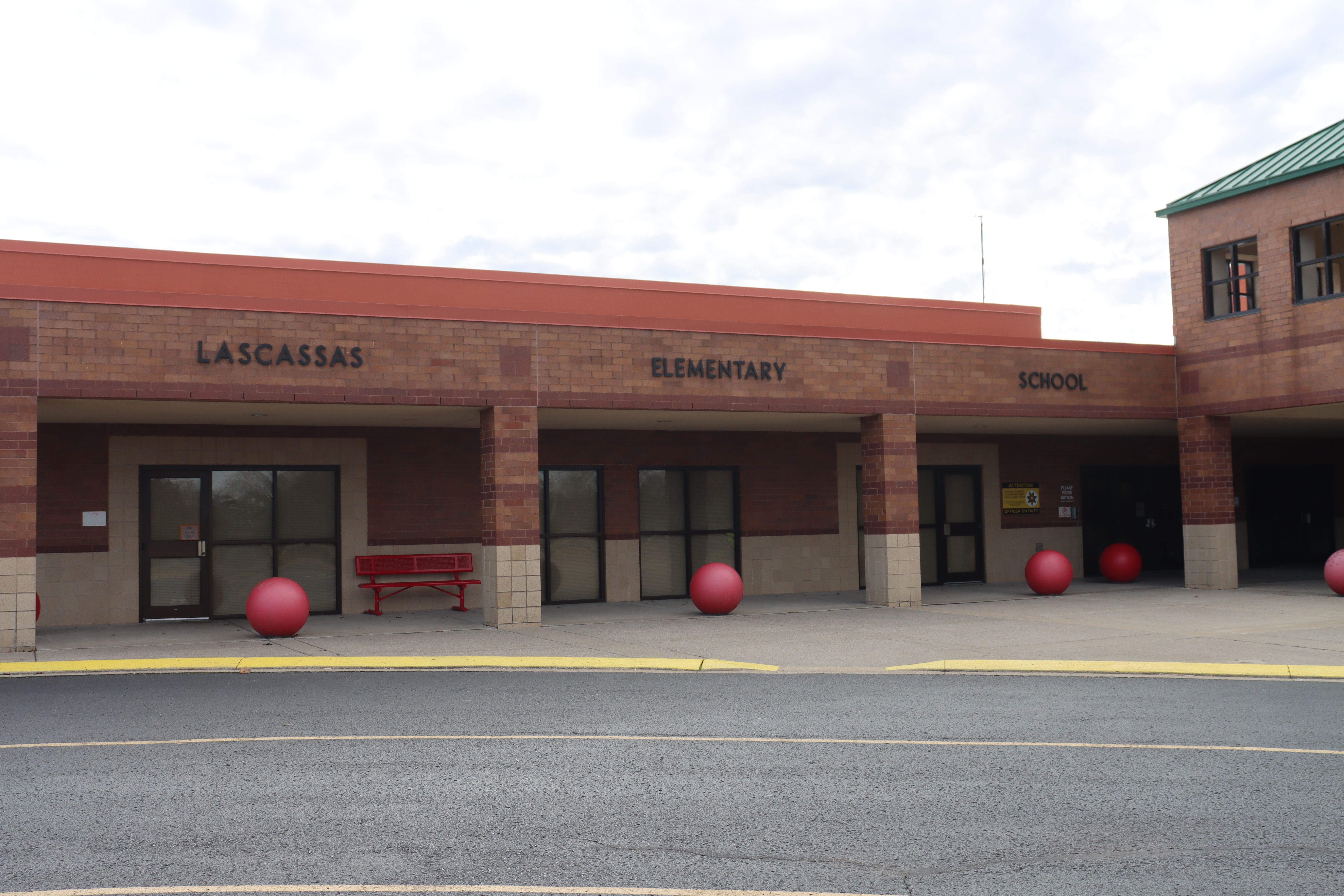 Red and brick elementary school exterior with a red roof. Red balls on the sidewalk. A red bench in front.