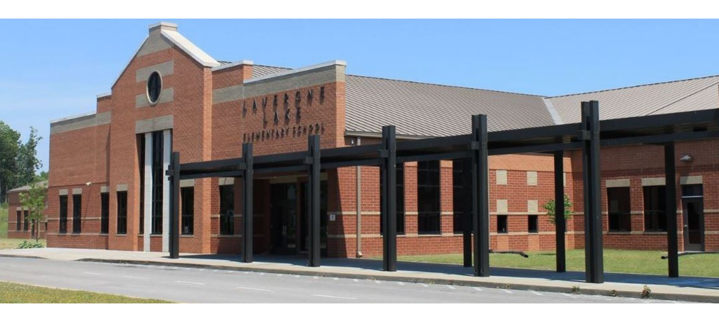 A large brick building with multiple windows and a gray roof. An entrance with a covered walkway.