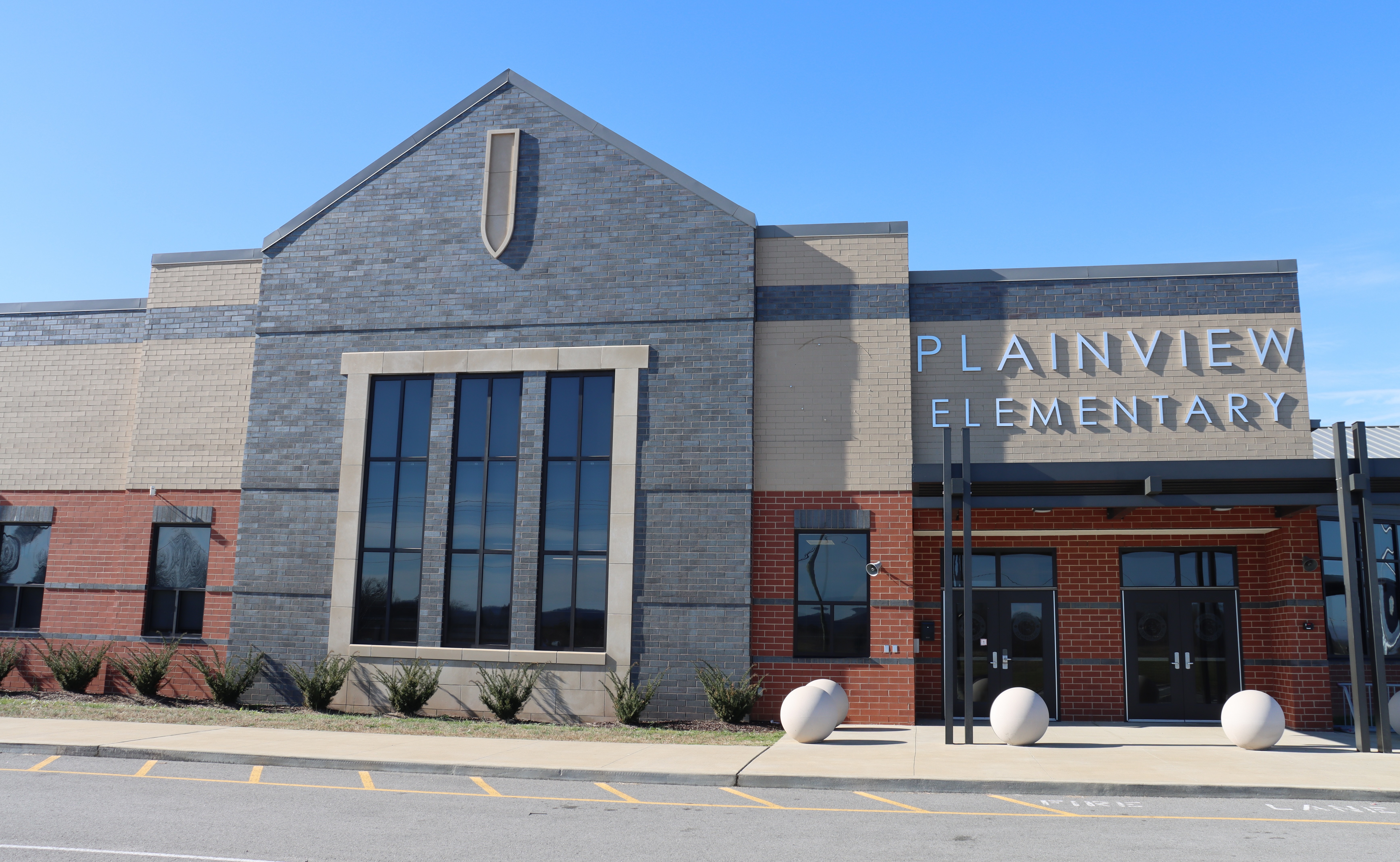 A modern building with "Plainview Elementary" on the front. Large windows, brick accents, and white globe lights.