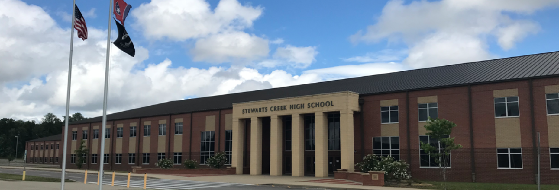 A school building with several columns and windows. Flags on poles in front. Blue sky with clouds.
