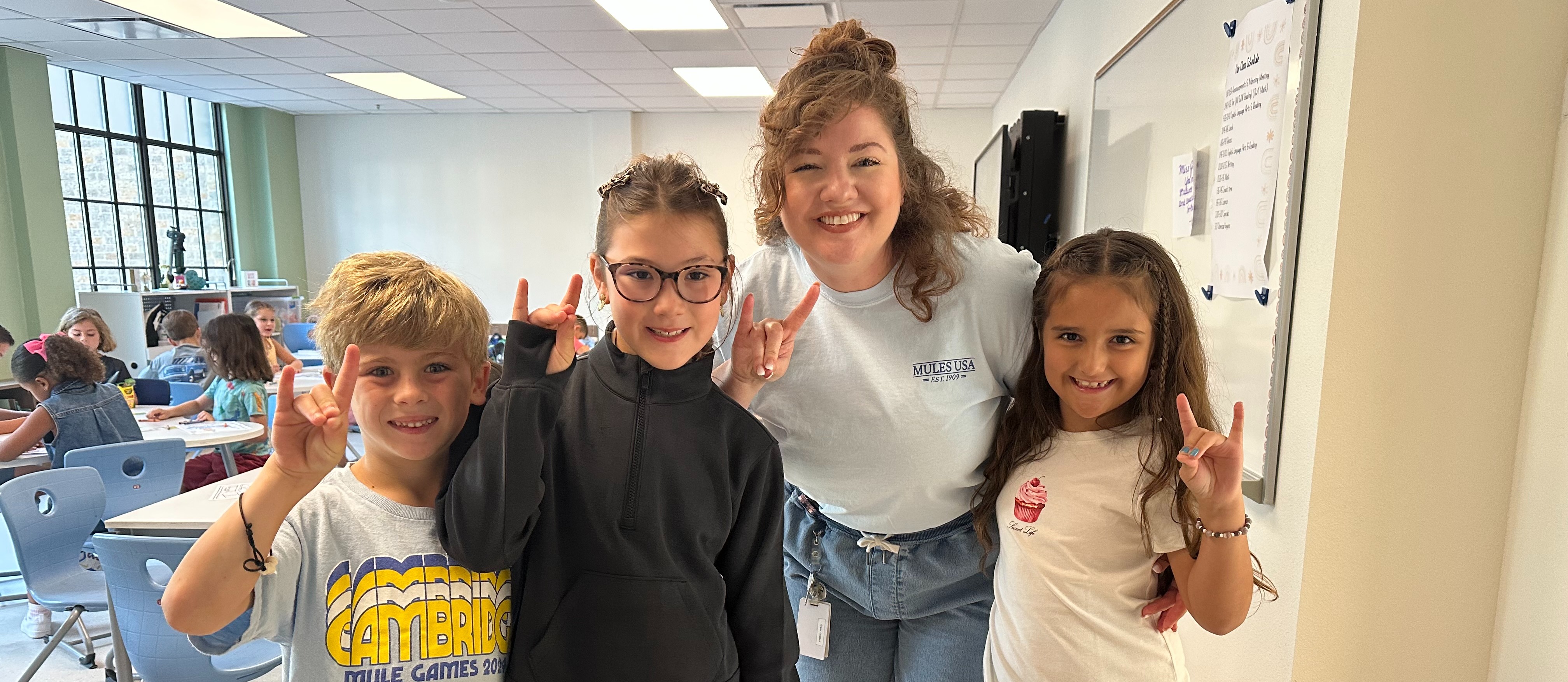 Teacher and three students smile and give Mules Up hand signal
