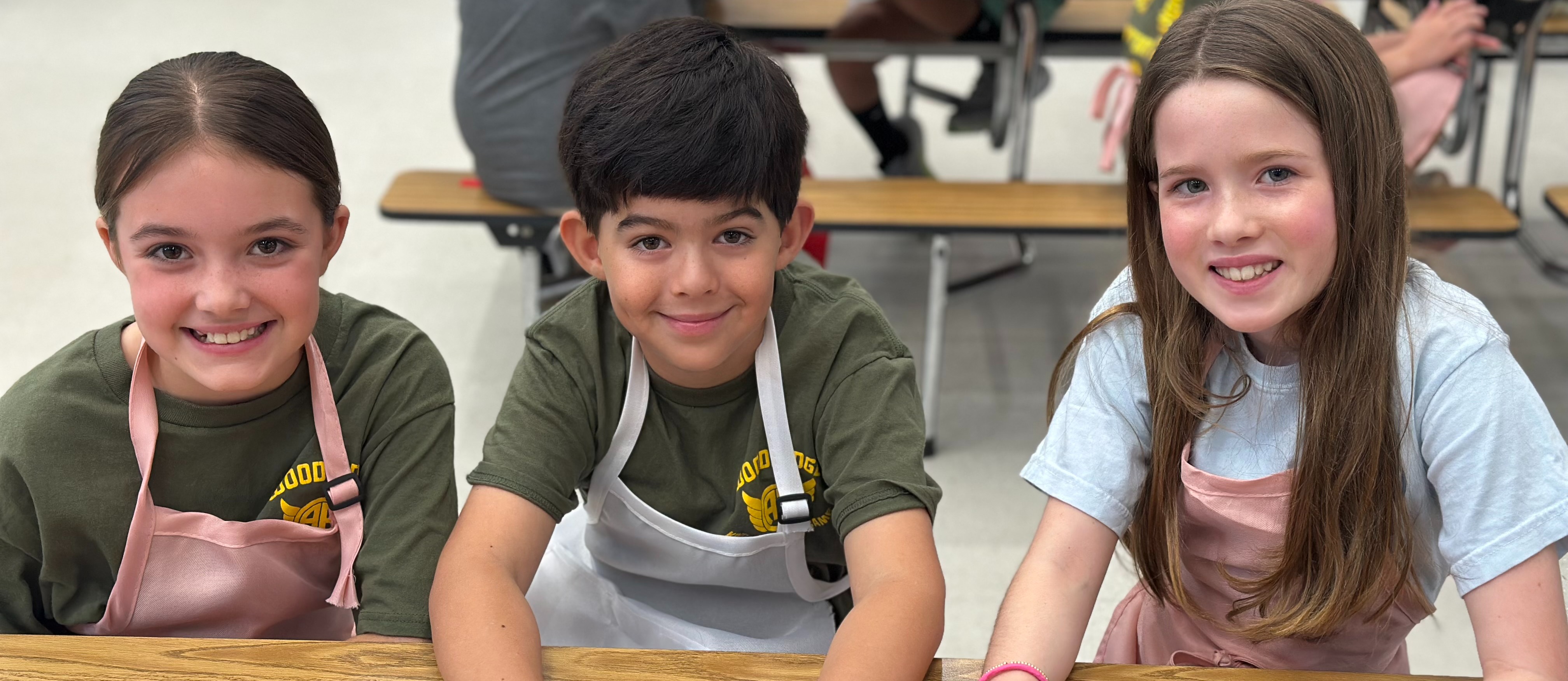 Three kids in aprons smiling at camera