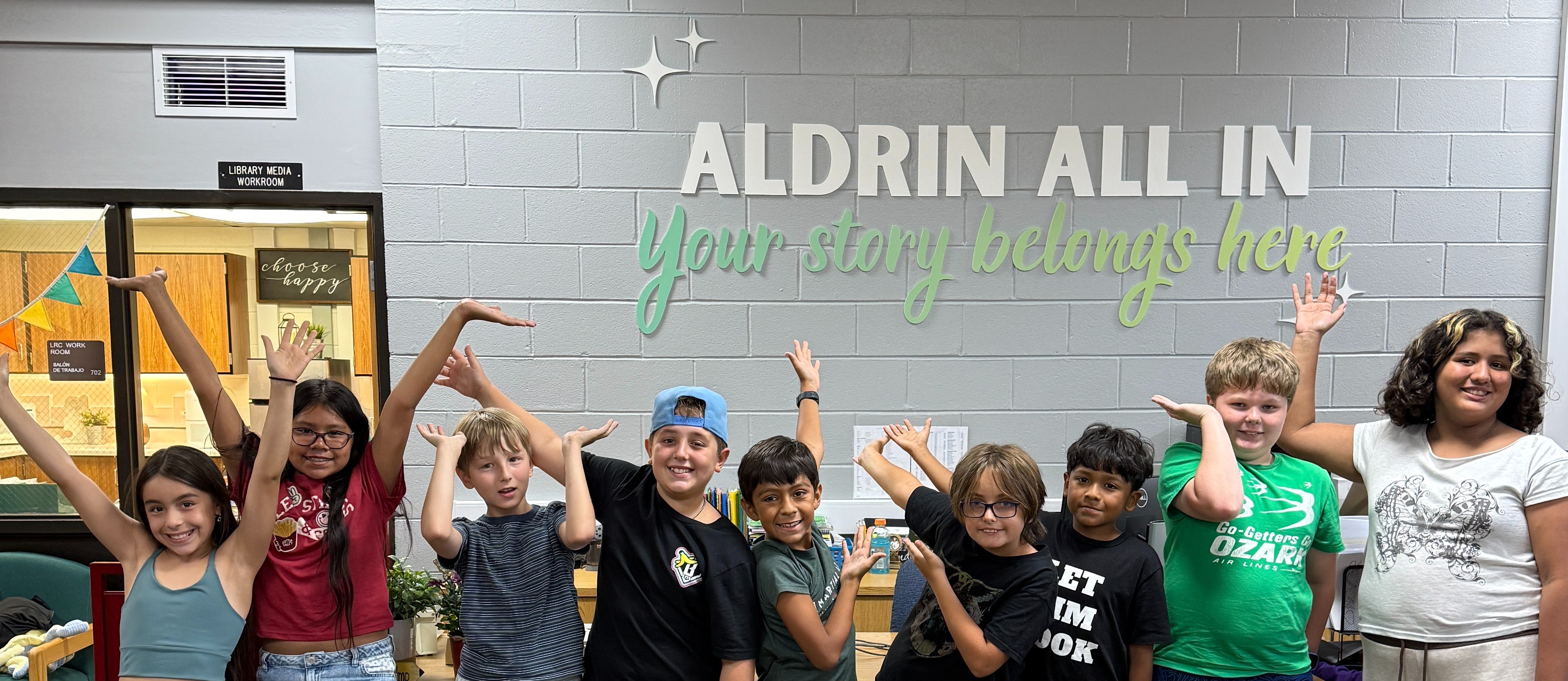 Students in front of our new library sign that says, "Aldrin All In. Your story belongs here."