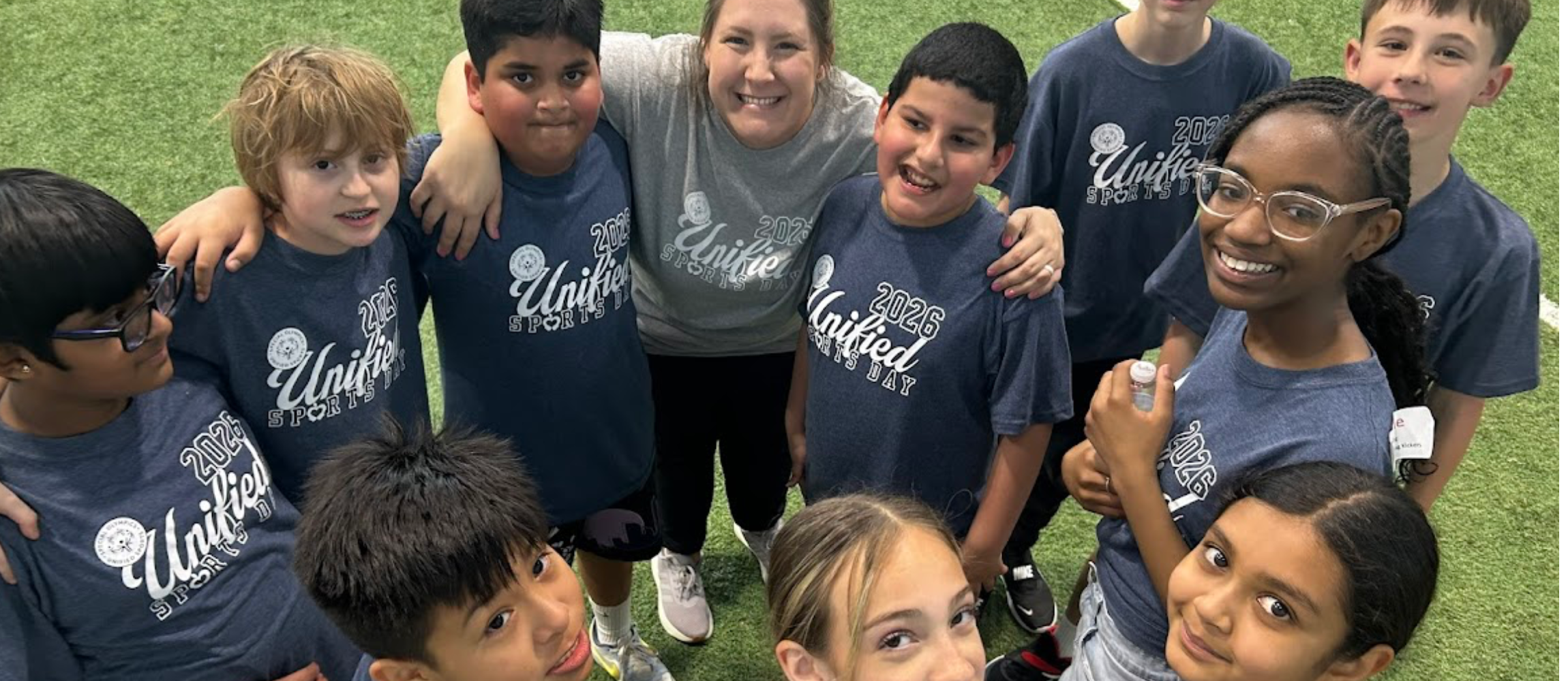 Students standing grass outside in gray shirts with a teacher smiling