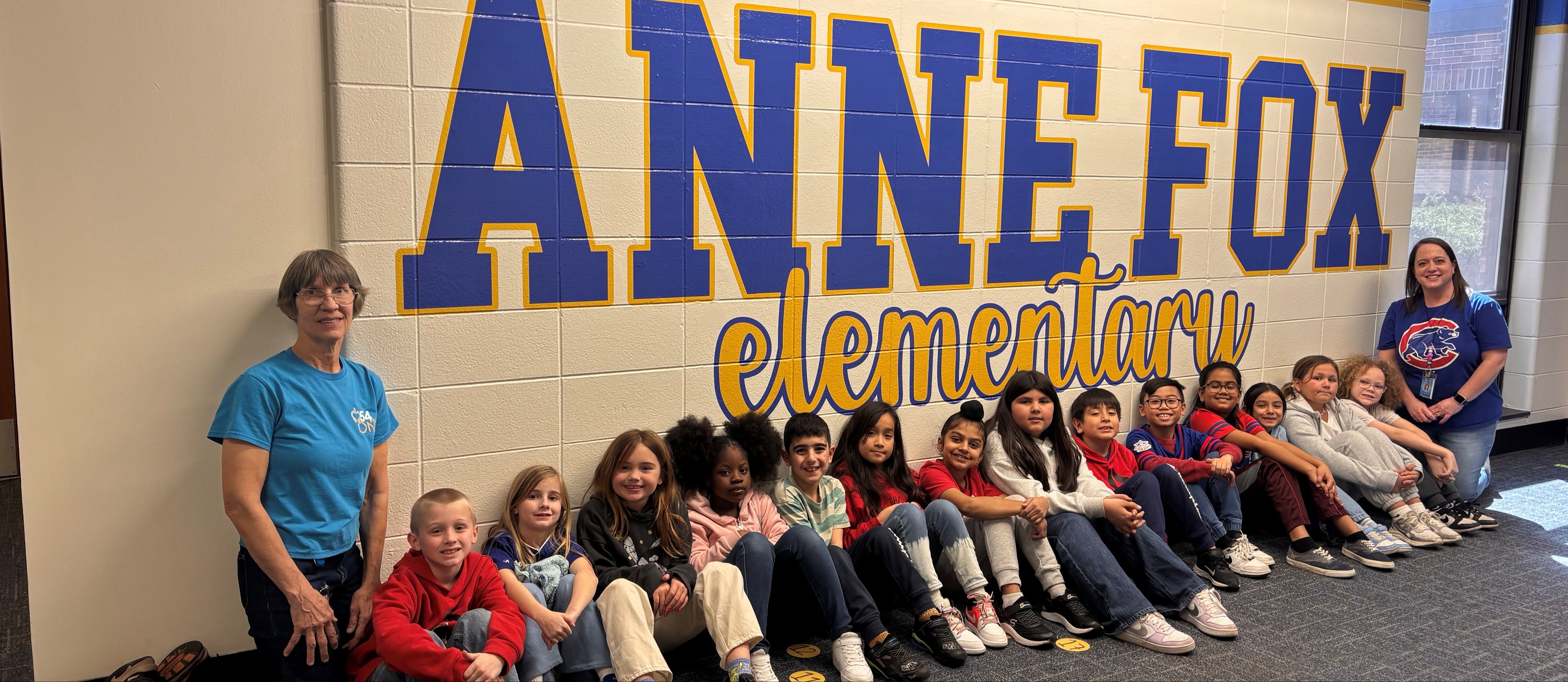 students sitting in front of a mural spelling Anne Fox Elementary