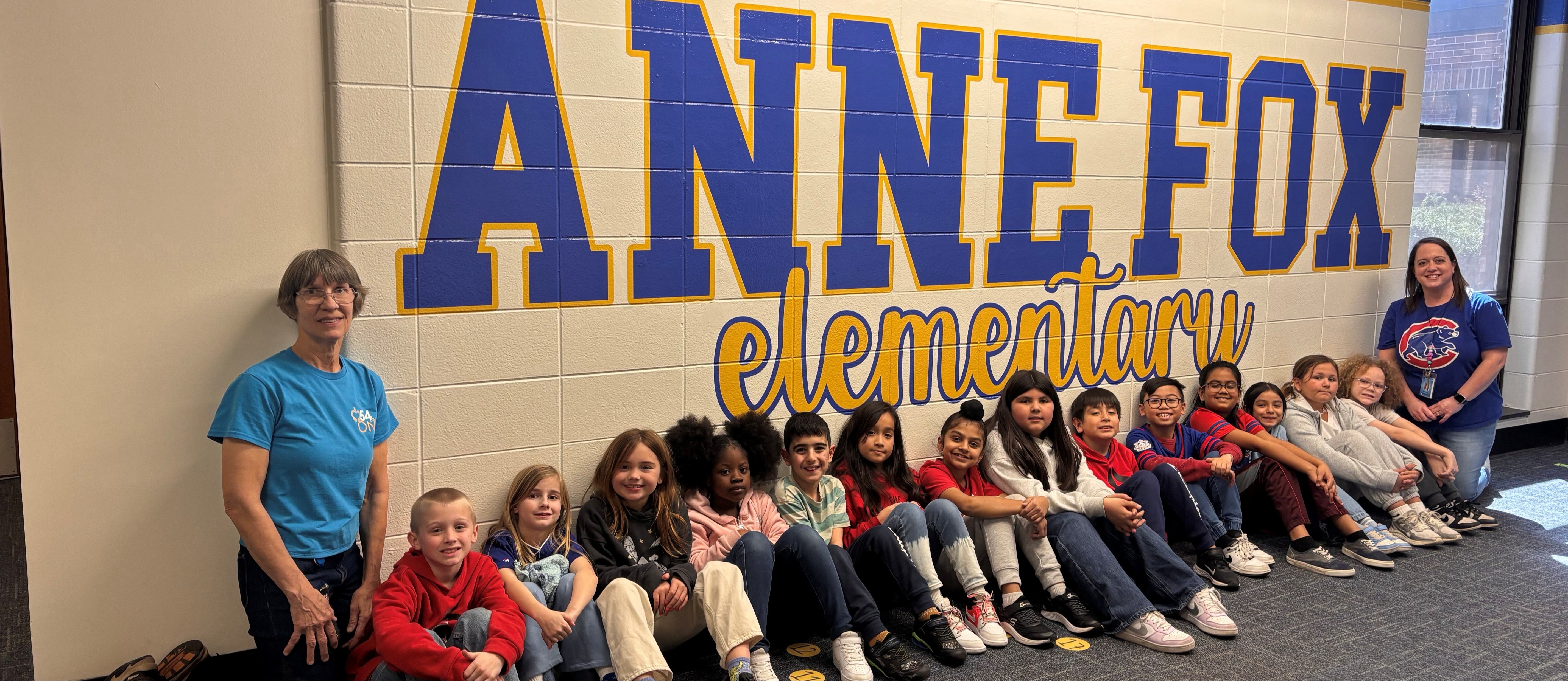 students sitting in front of a mural spelling Anne Fox Elementary
