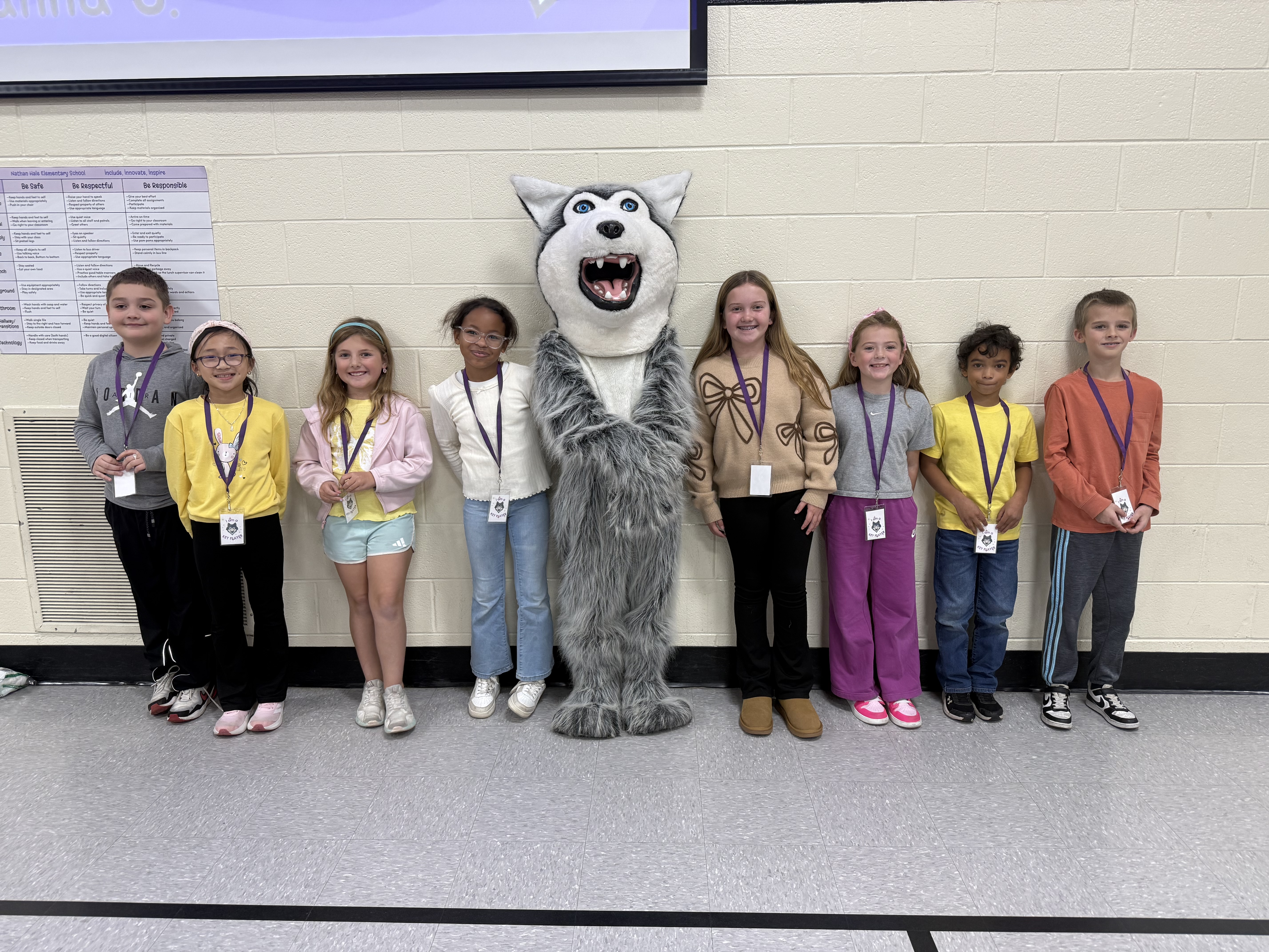Students standing against a white wall with the Shadow the Wolf Mascot